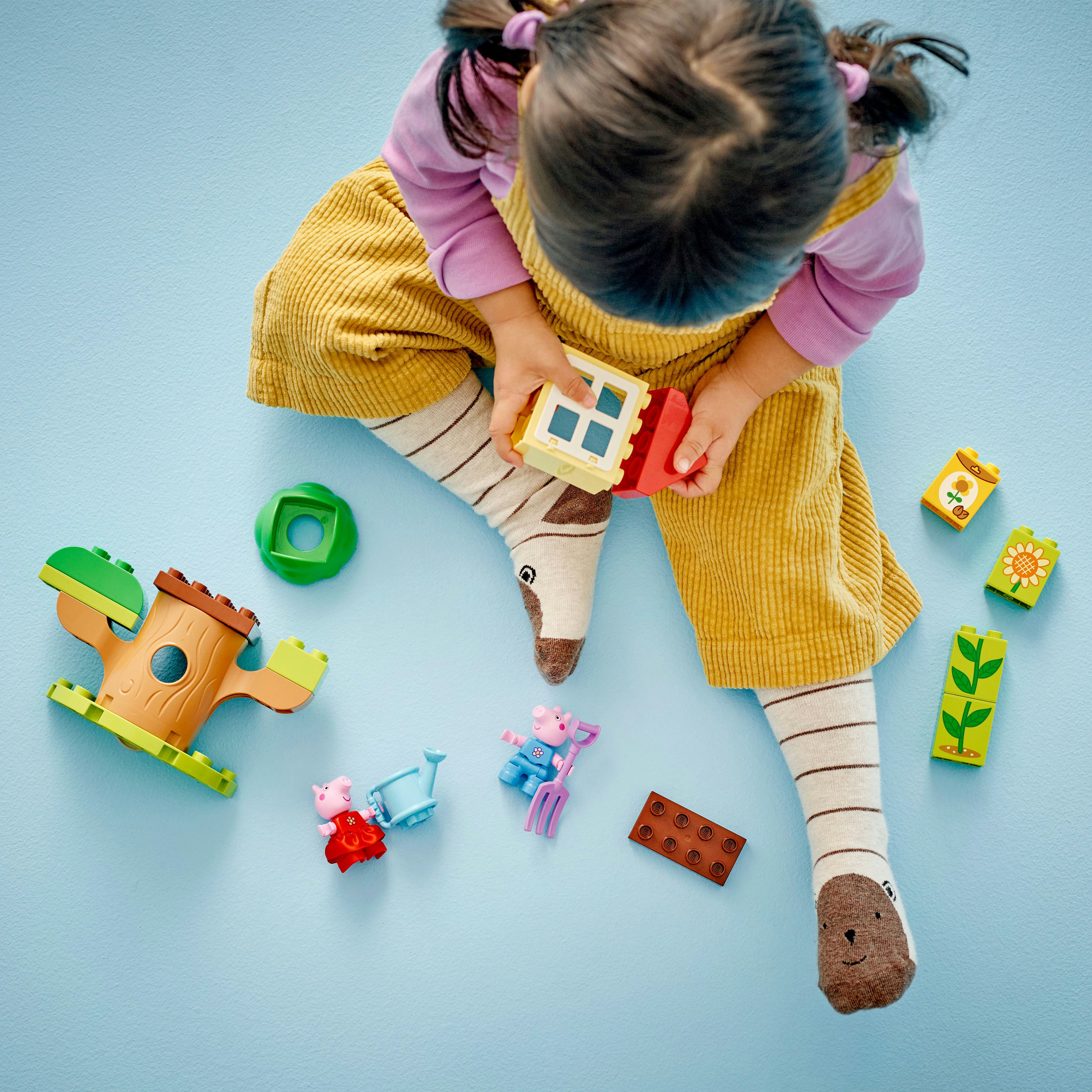 Dziecko bawiące się klockami Lego Duplo. Klocki obejmują drzewo, świnki i kwiaty.