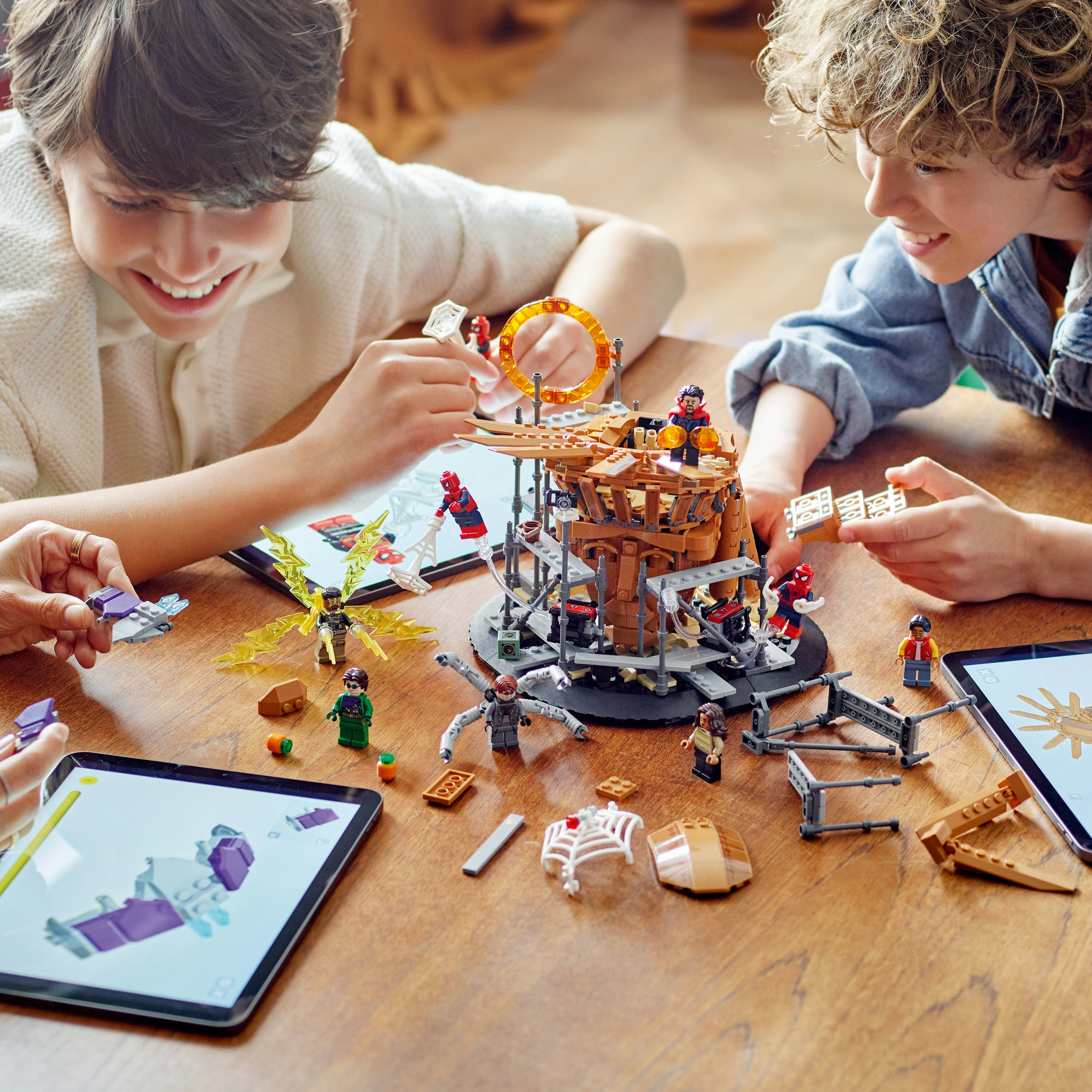 Dos niños construyendo un set de Lego, con piezas de Lego y una tableta sobre una mesa de madera.