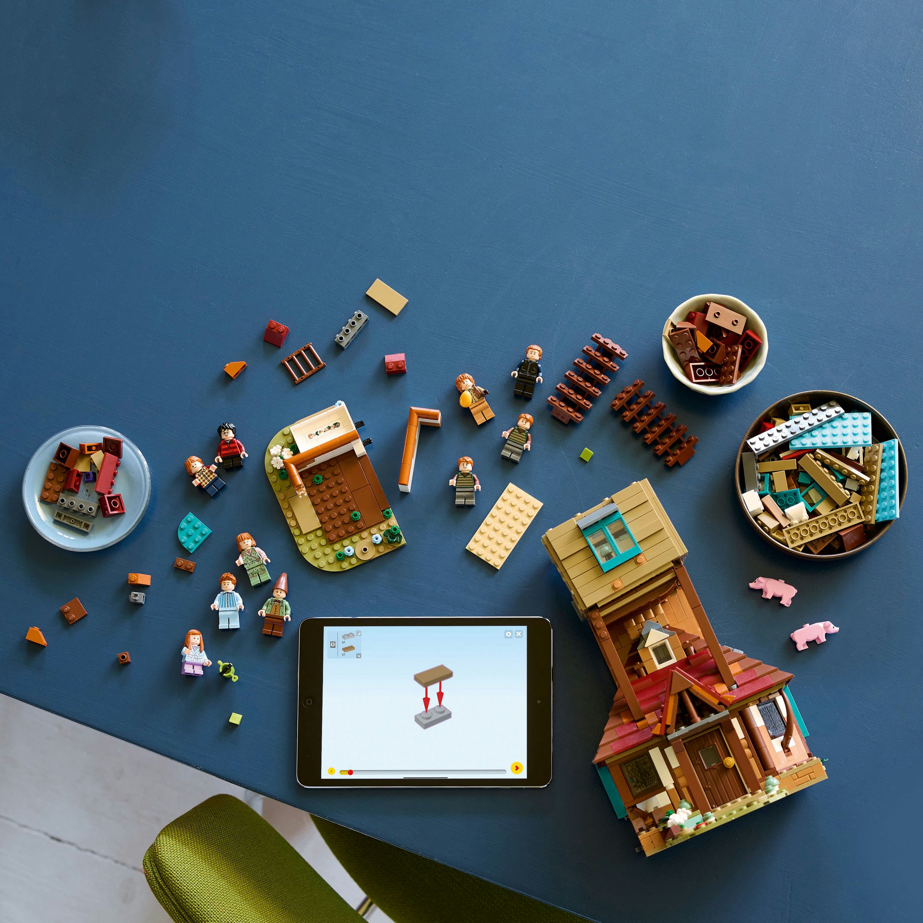 Zestaw Lego ze złożonymi budynkami i figurkami na niebieskiej powierzchni. Zawiera tablet pokazujący etapy budowy.