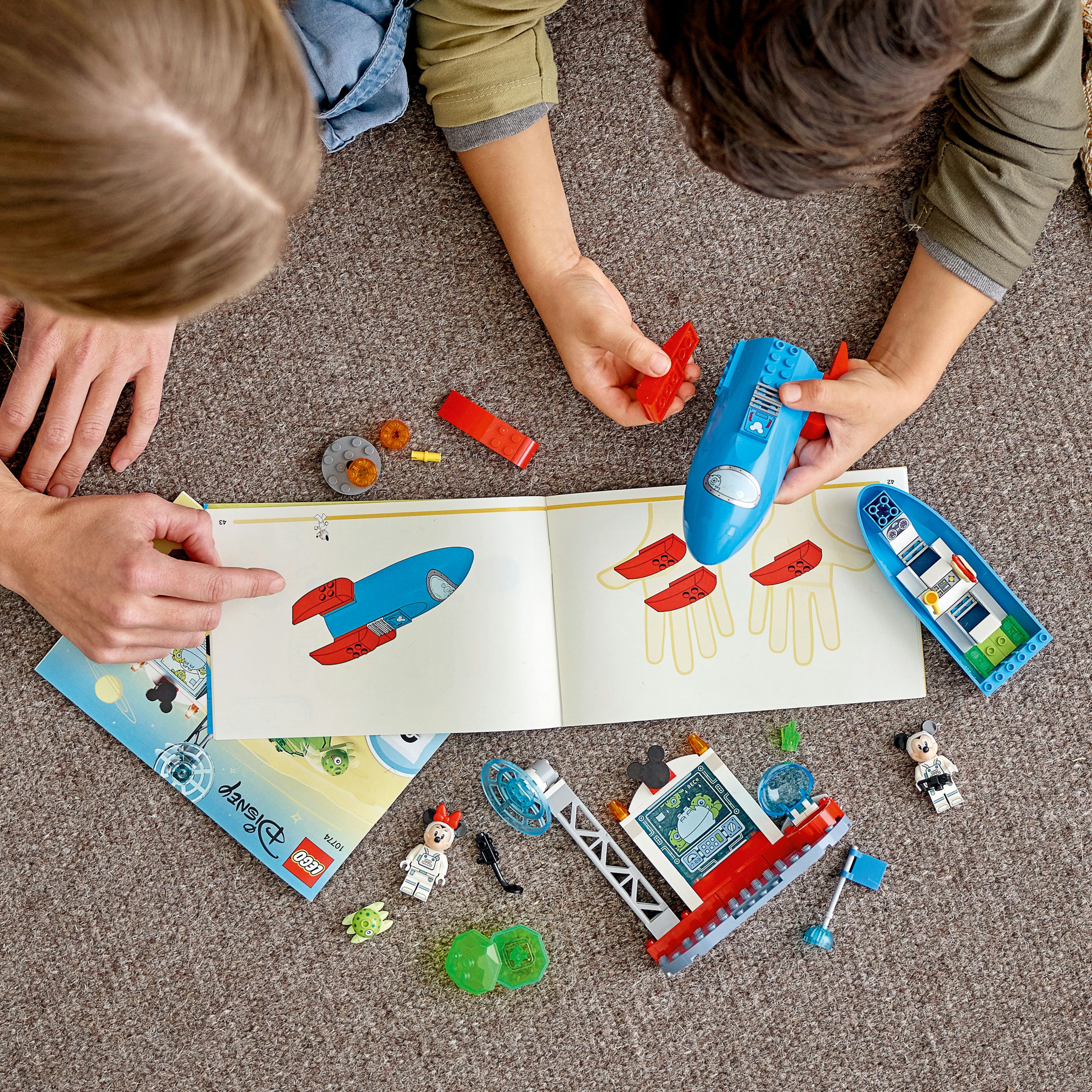 Zwei Kinder bauen Lego, Anleitung offen, verschiedene Legoteile auf Teppich.