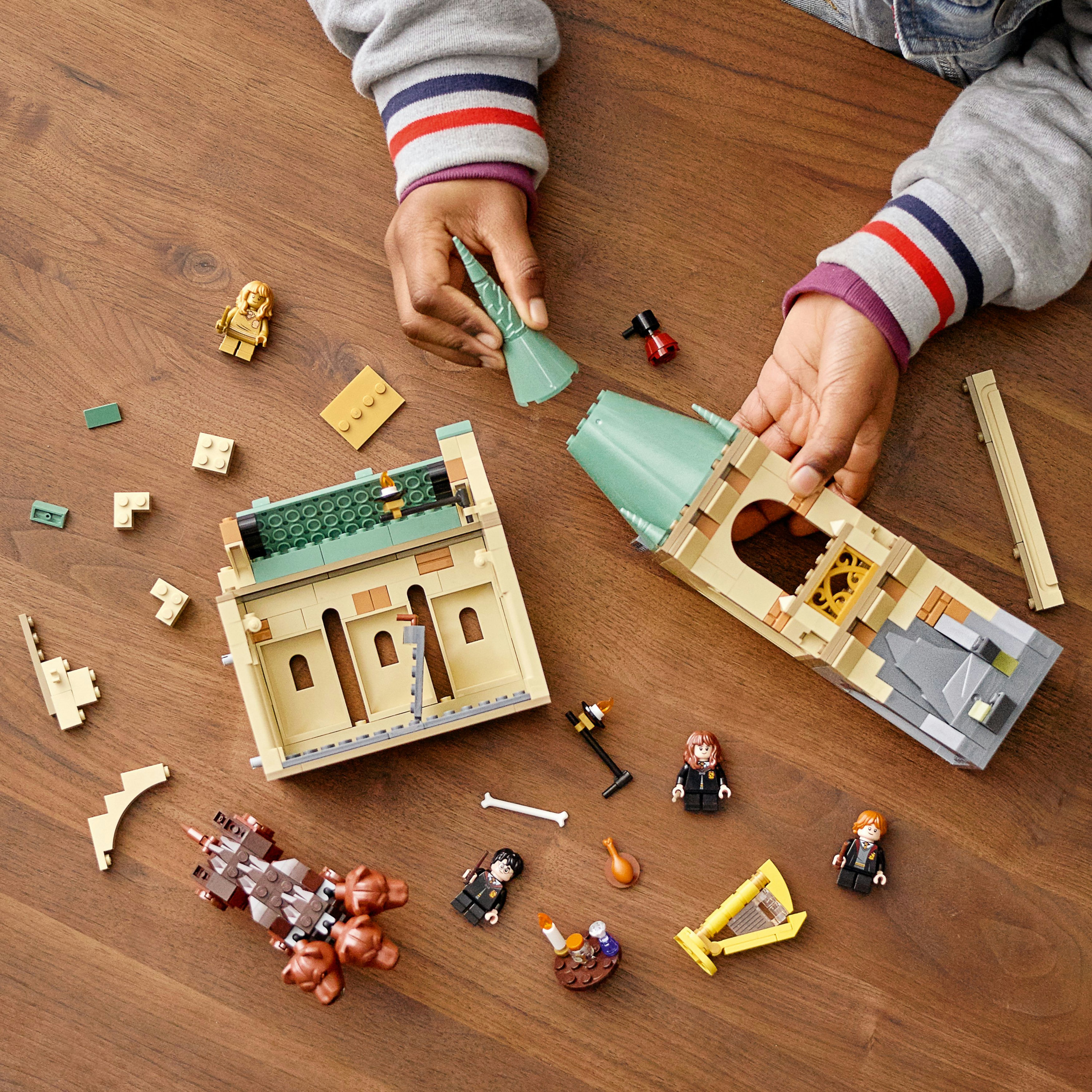 Mani di bambino che costruiscono il set LEGO Hogwarts, con varie figure e pezzi su una superficie di legno.