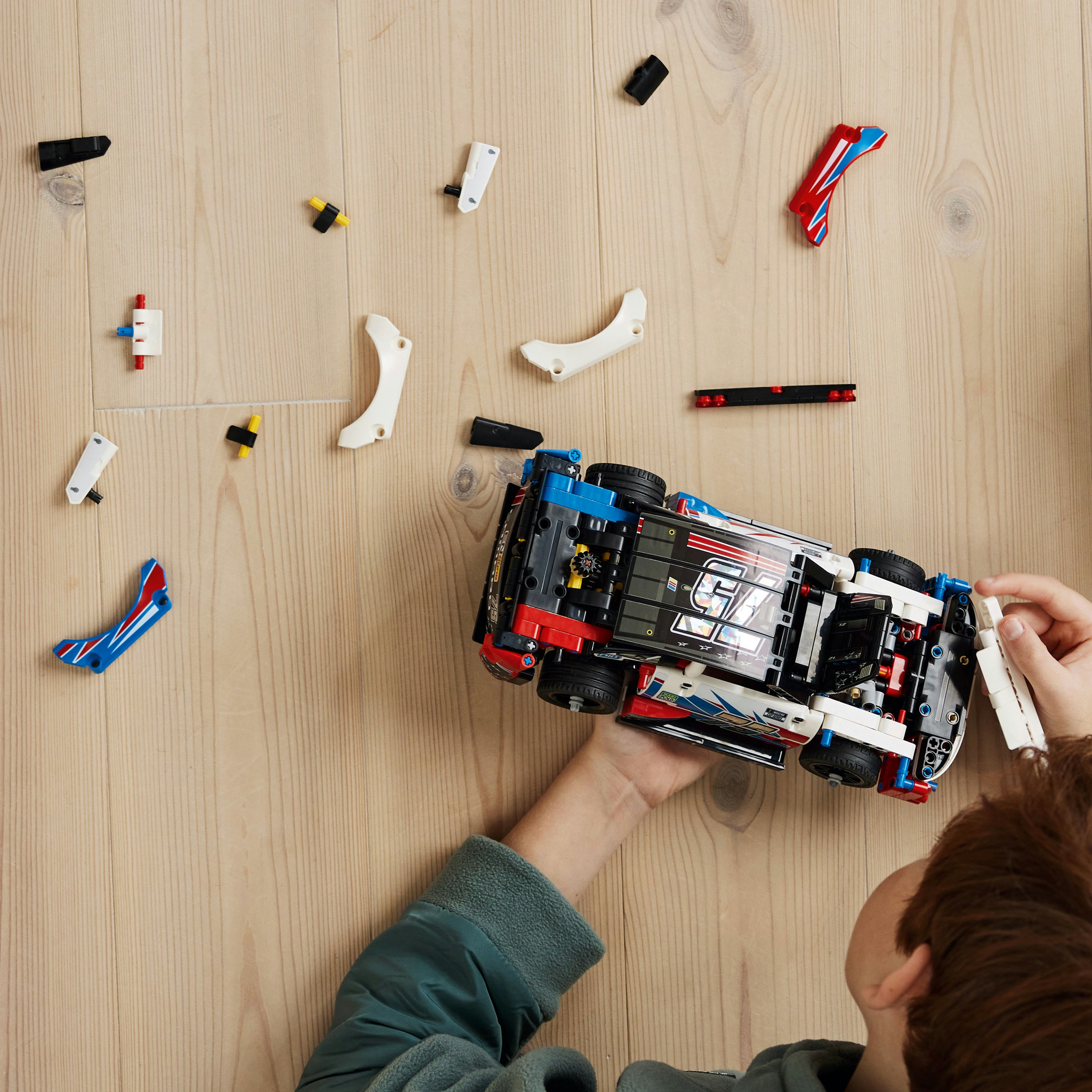 Een kind monteert een Lego raceauto. Onderdelen verspreid op een houten oppervlak.