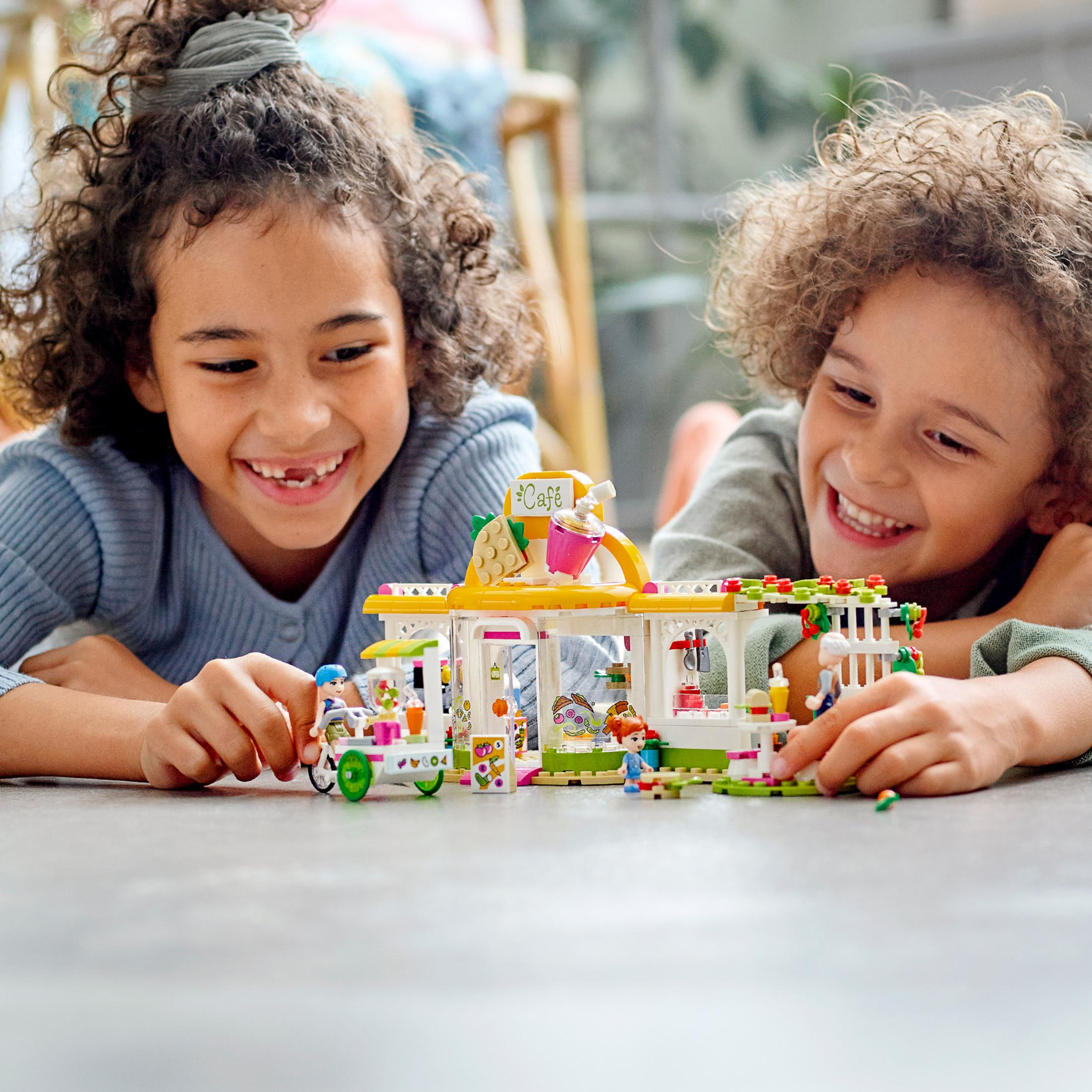Due bambini che costruiscono un bar Lego. Il bar è giallo, bianco e verde con un'insegna rosa.