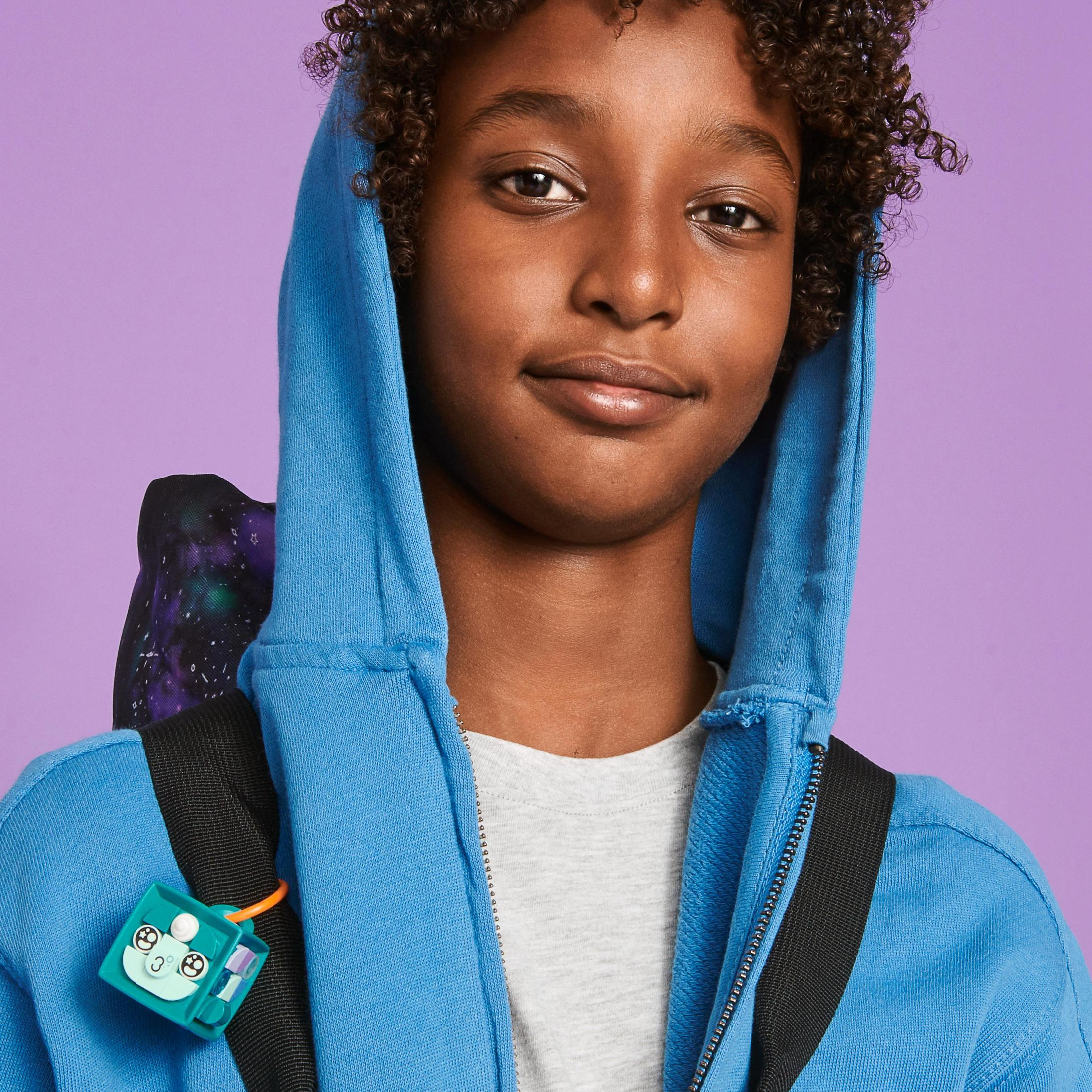 Ein junger Junge in einem blauen Kapuzenpullover mit Rucksack und kleinem Spielzeug.