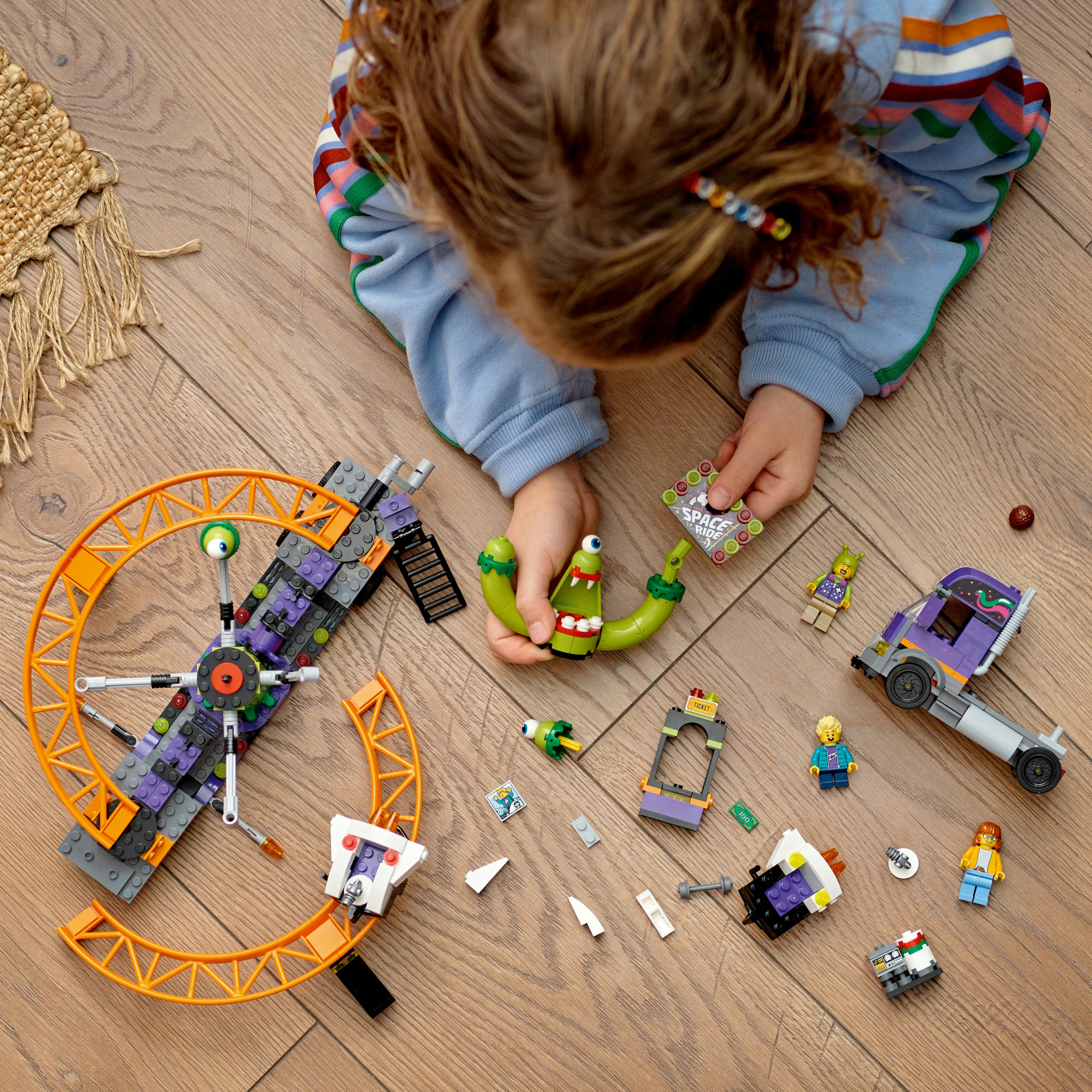Dziecko bawiące się Lego, z kolejką górską, samochodem i minifigurkami rozrzuconymi na drewnianej podłodze.