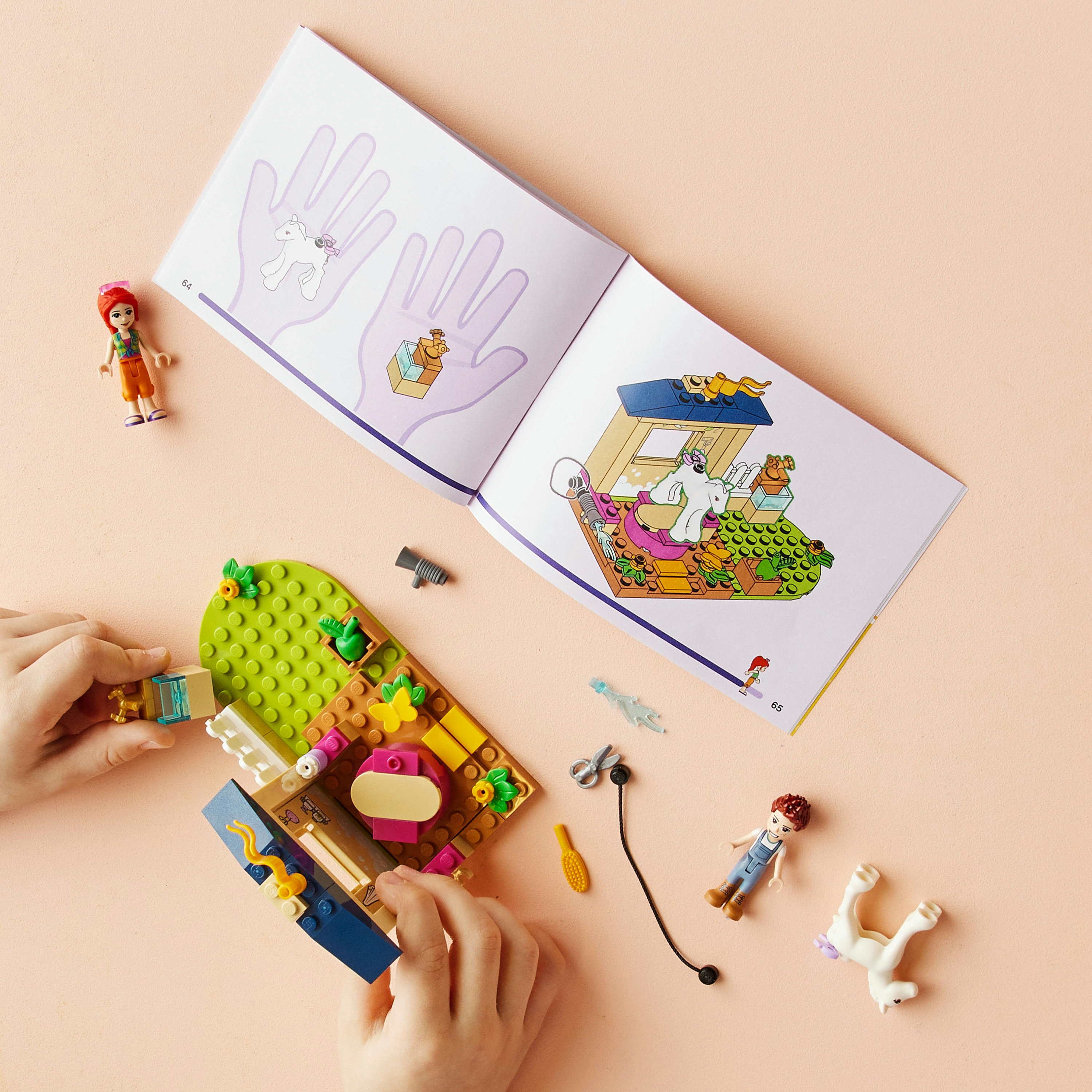 Handen die met Lego-stukken en een handleiding spelen. De achtergrond is een lichtroze oppervlak.