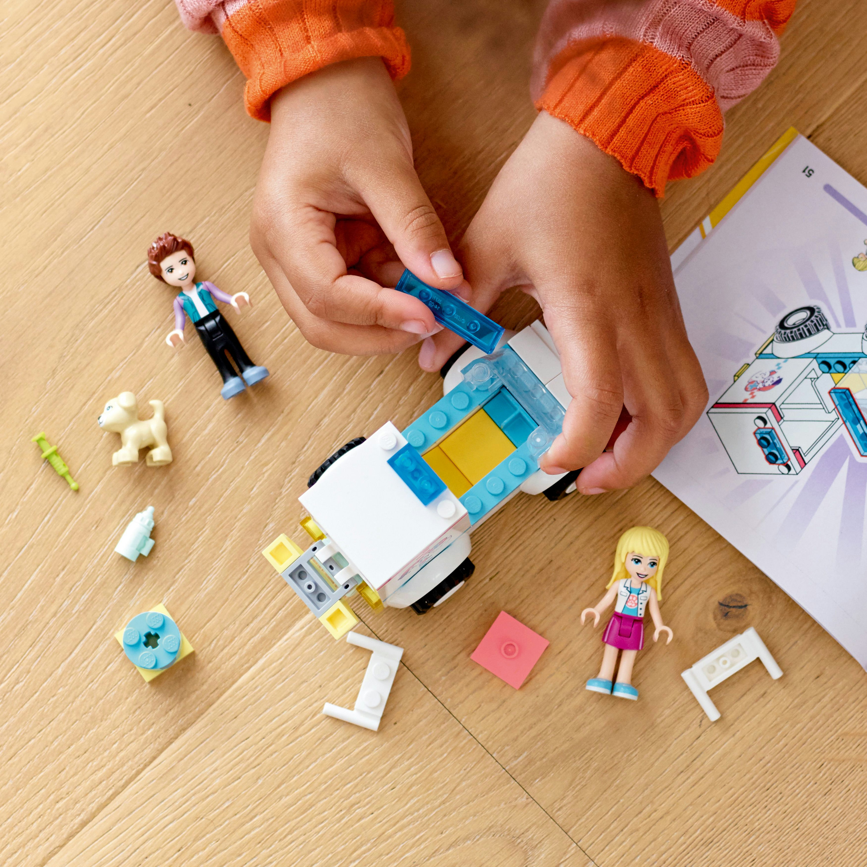 Hände, die ein weißes Automodell mit Lego-Teilen zusammensetzen. Verschiedene Lego-Figuren und -Teile sind verstreut.