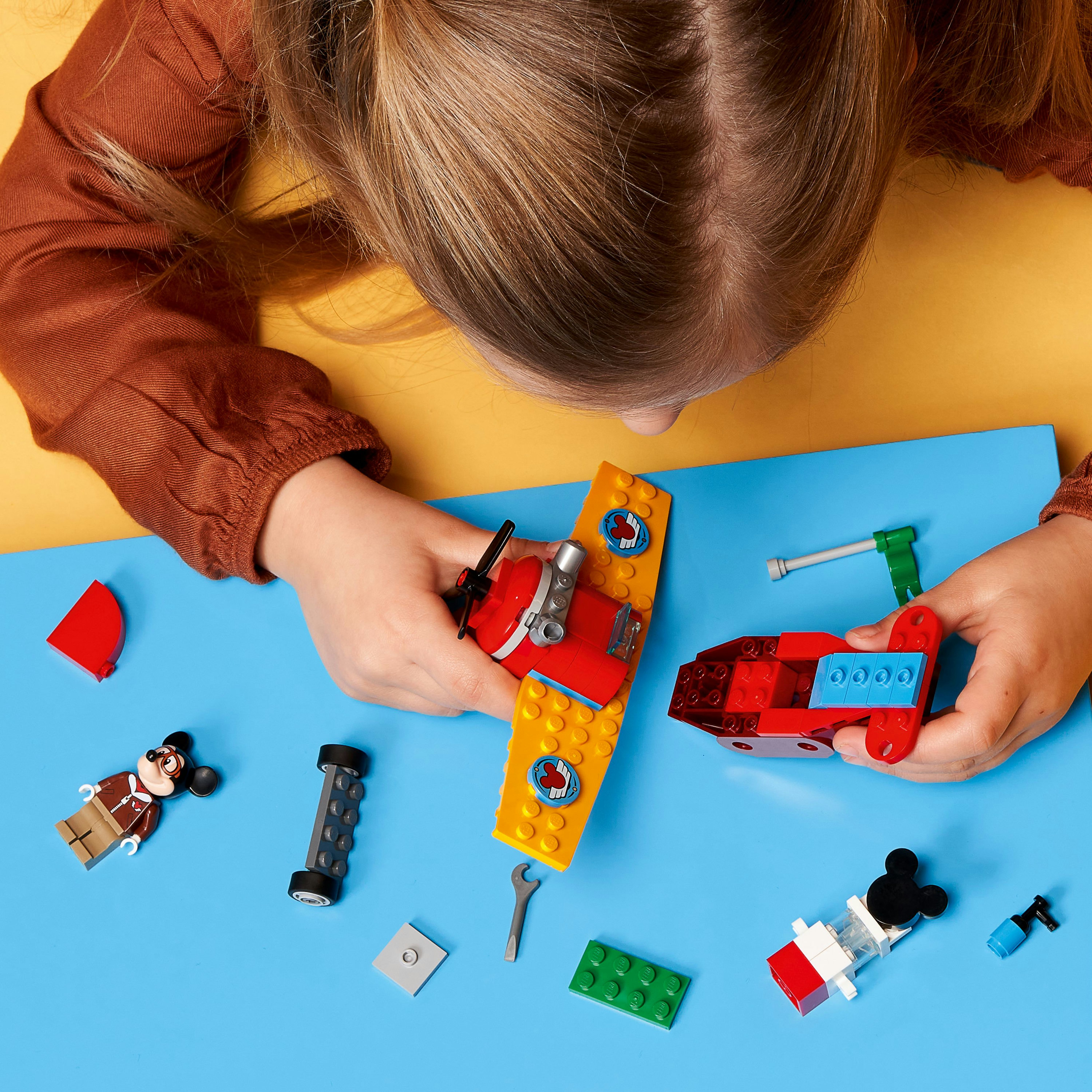 Dziecko składające samolot Lego, z różnymi częściami i figurkami Myszki Miki.