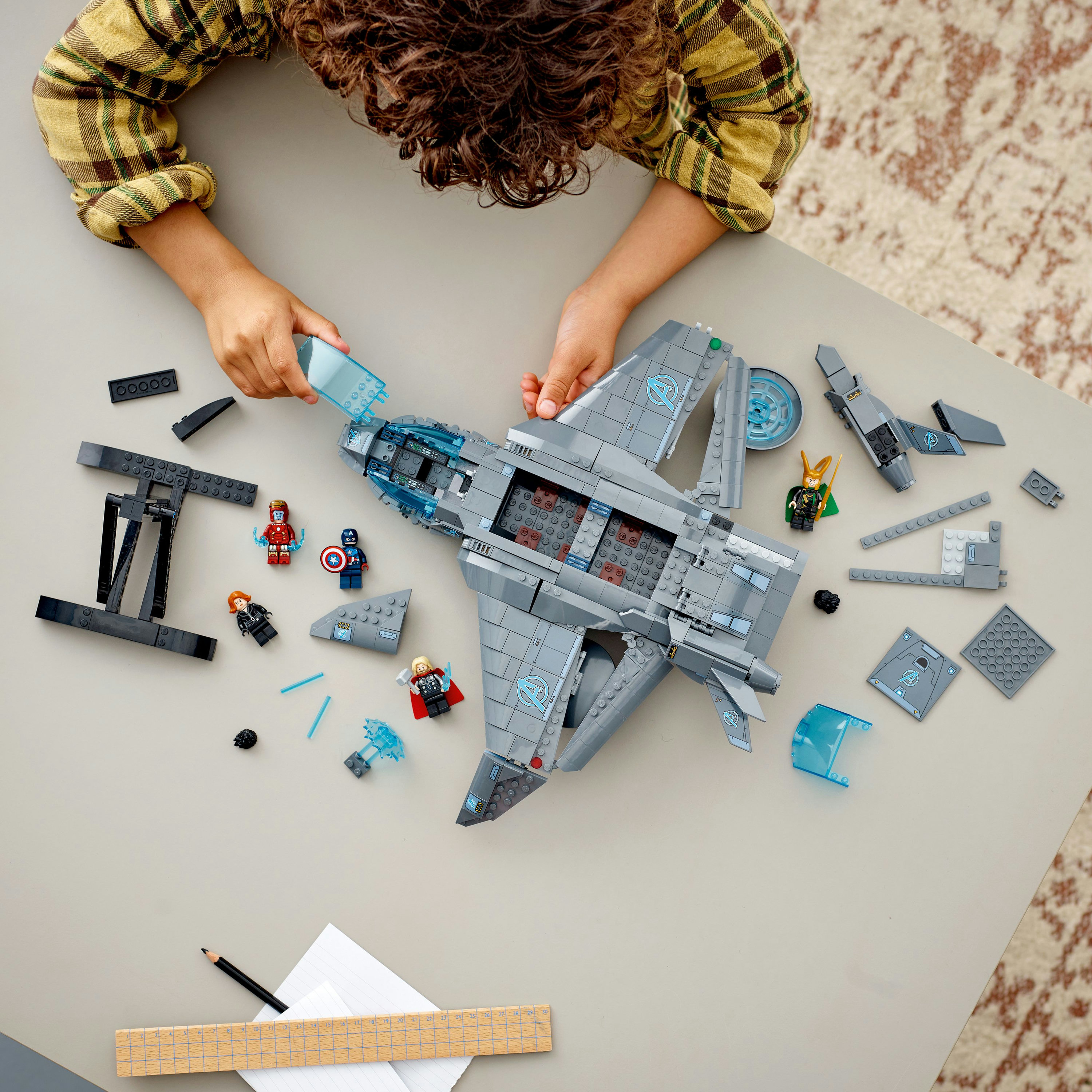 Ein Kind baut ein graues LEGO-Jet mit Minifiguren auf einem Tisch zusammen.