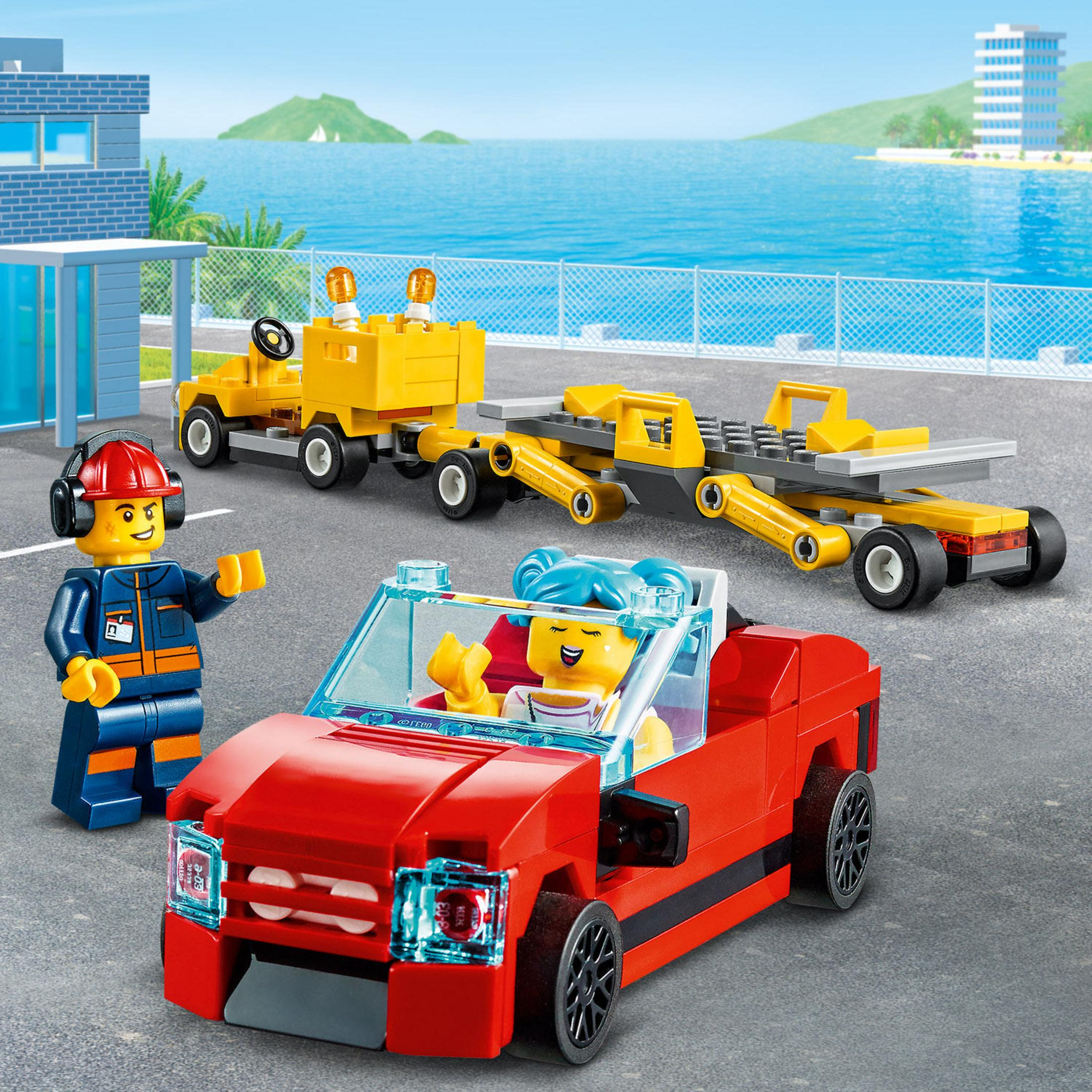 Scena Lego City z czerwonym kabrioletem, żółtą lawetą i figurkami, z widokiem na morze.