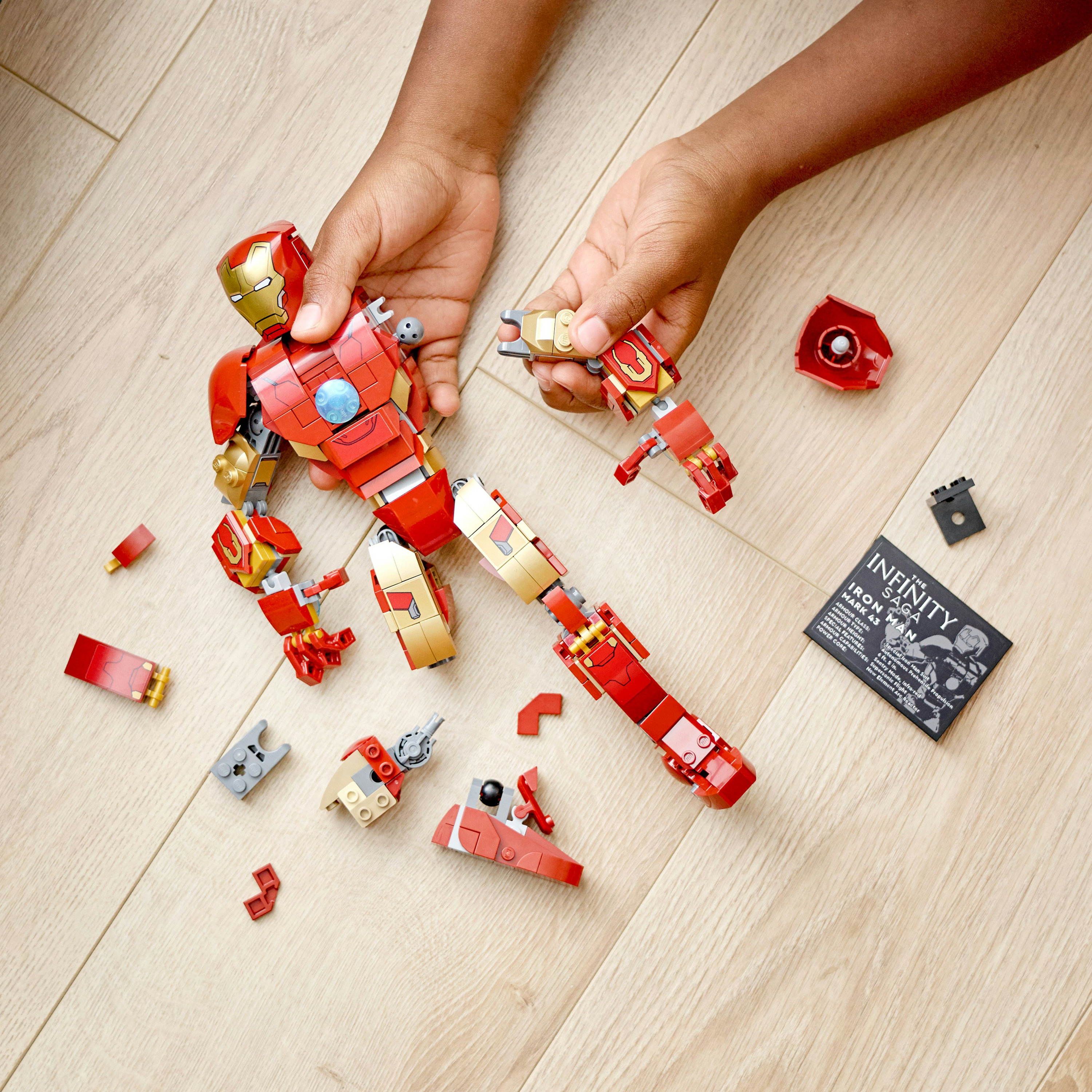 Mani che assemblano una figura Lego Iron Man, con pezzi sparsi sul legno.