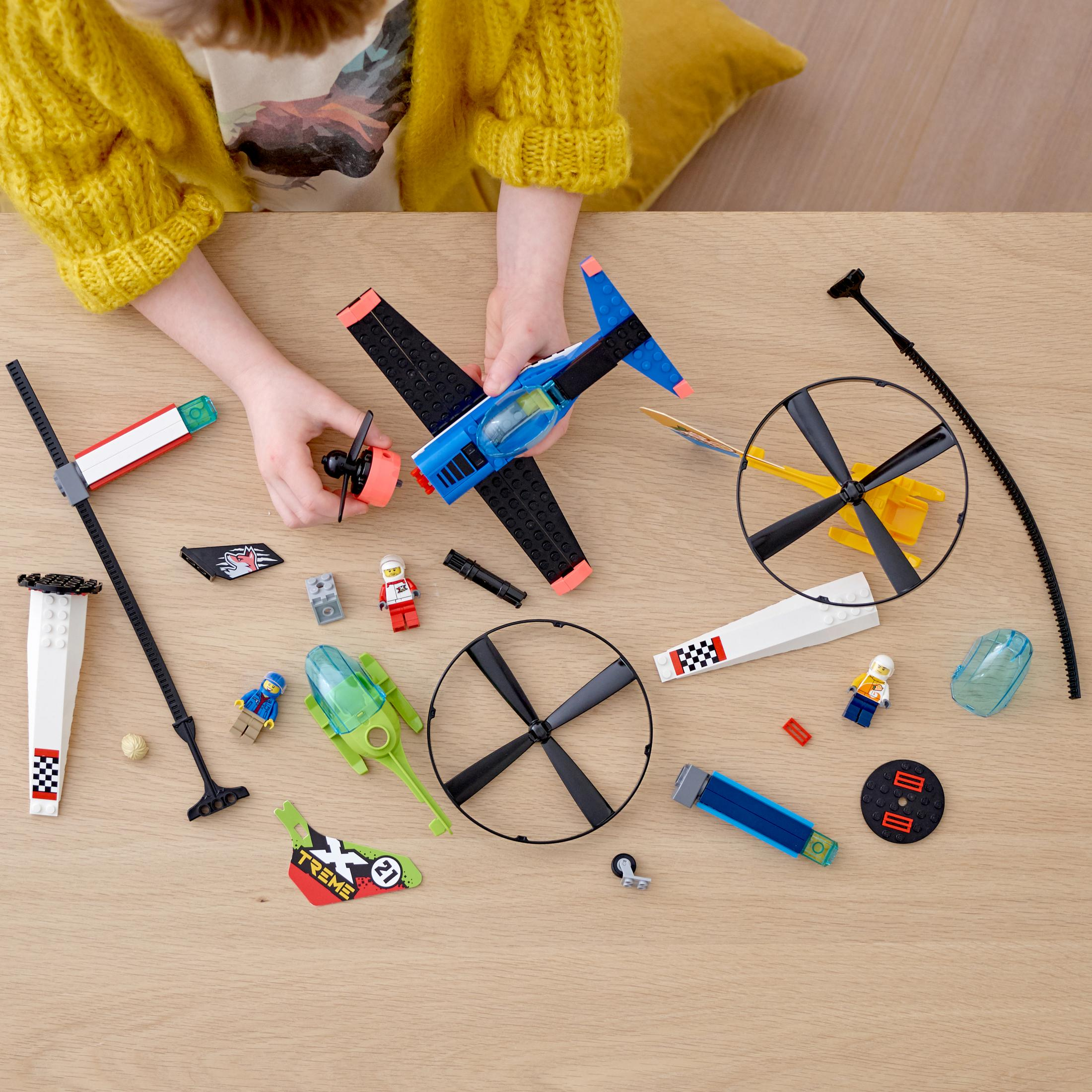 Kinderhände halten ein blaues und schwarzes Spielzeugflugzeug. Viele Flugzeugteile und Mini-Figuren liegen auf dem Tisch.