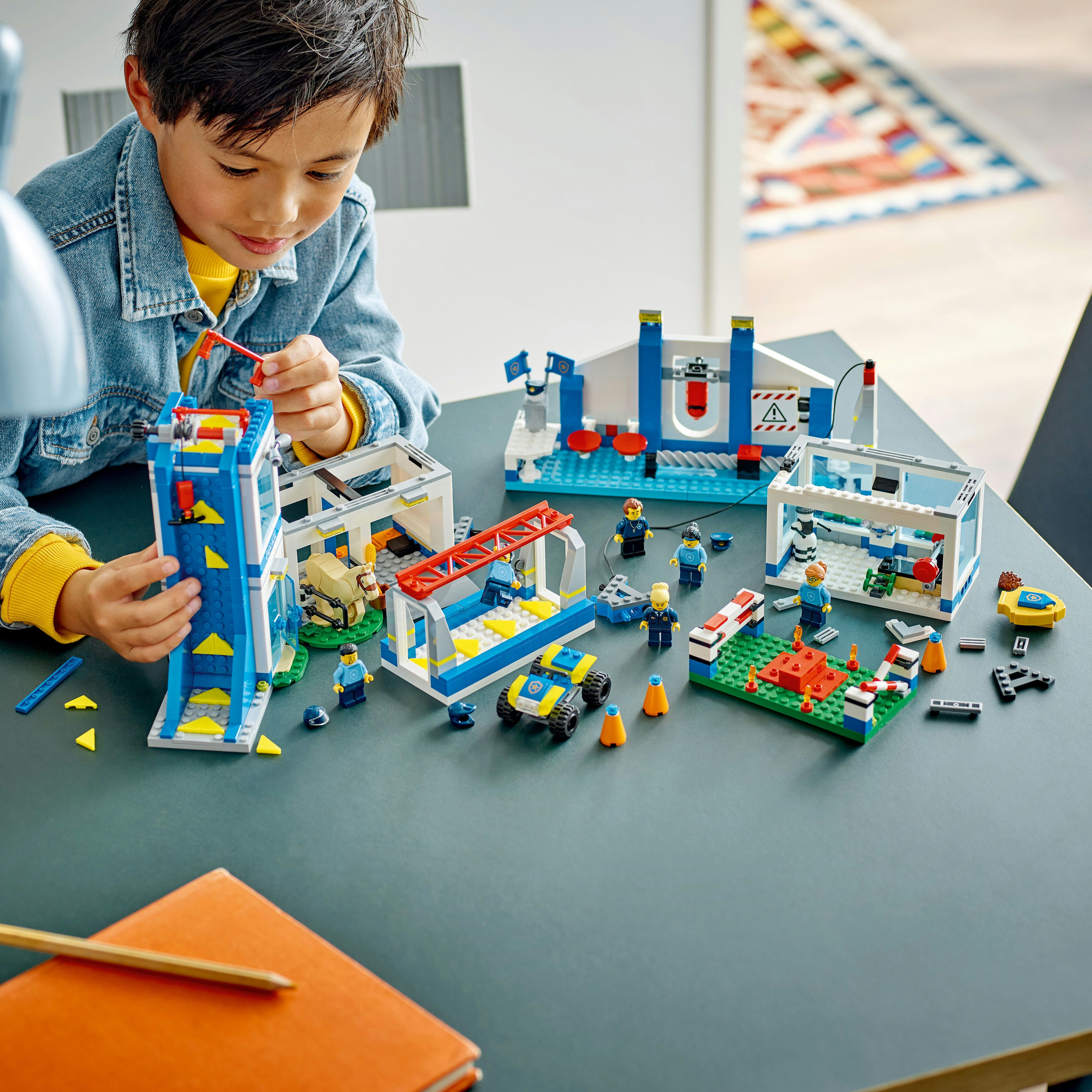 Ein Kind spielt mit einem LEGO-Set mit Gebäudestrukturen und Figuren auf einem Tisch.