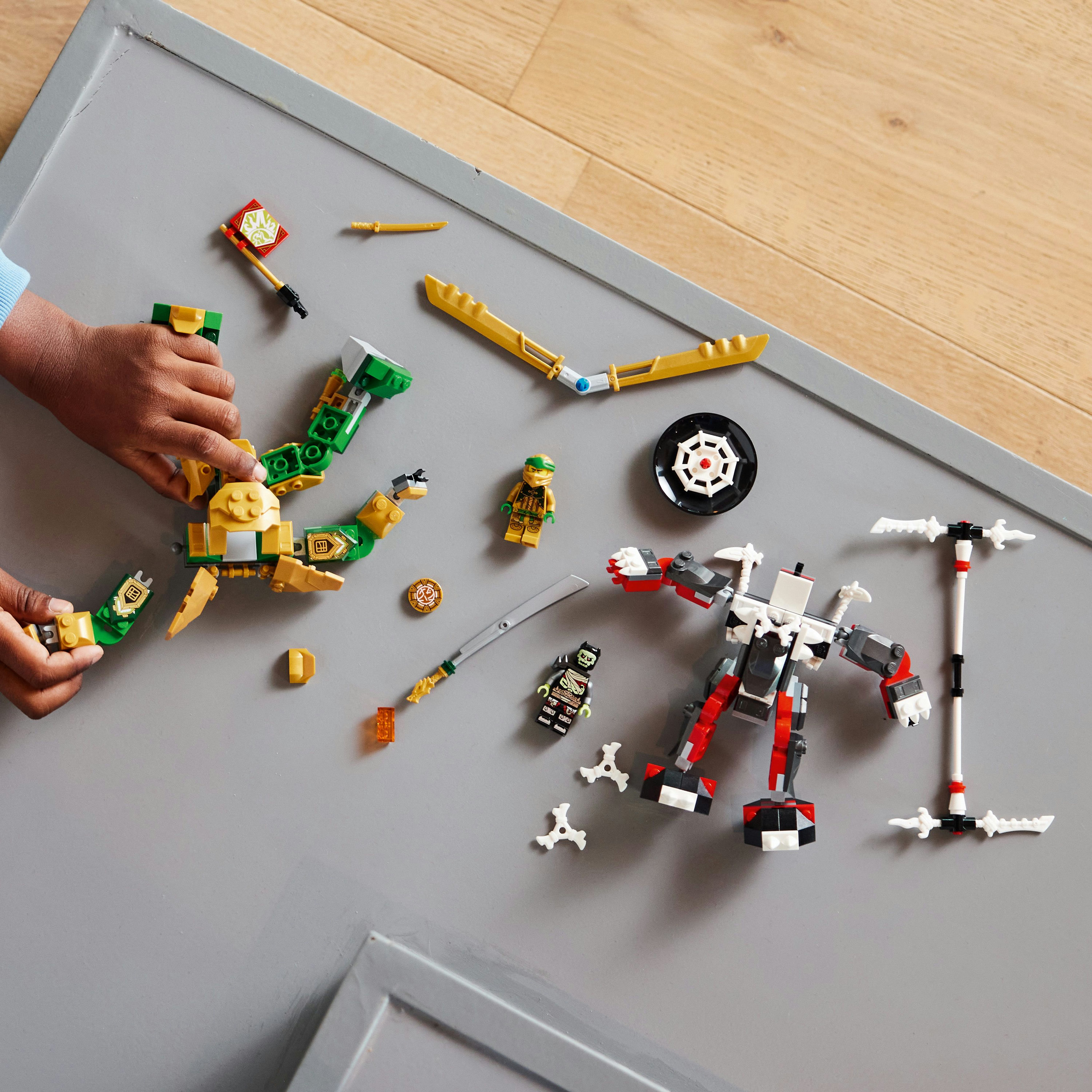 Set LEGO Ninjago: Mani che assemblano un robot ninja con armi e vari pezzi Lego sparsi.