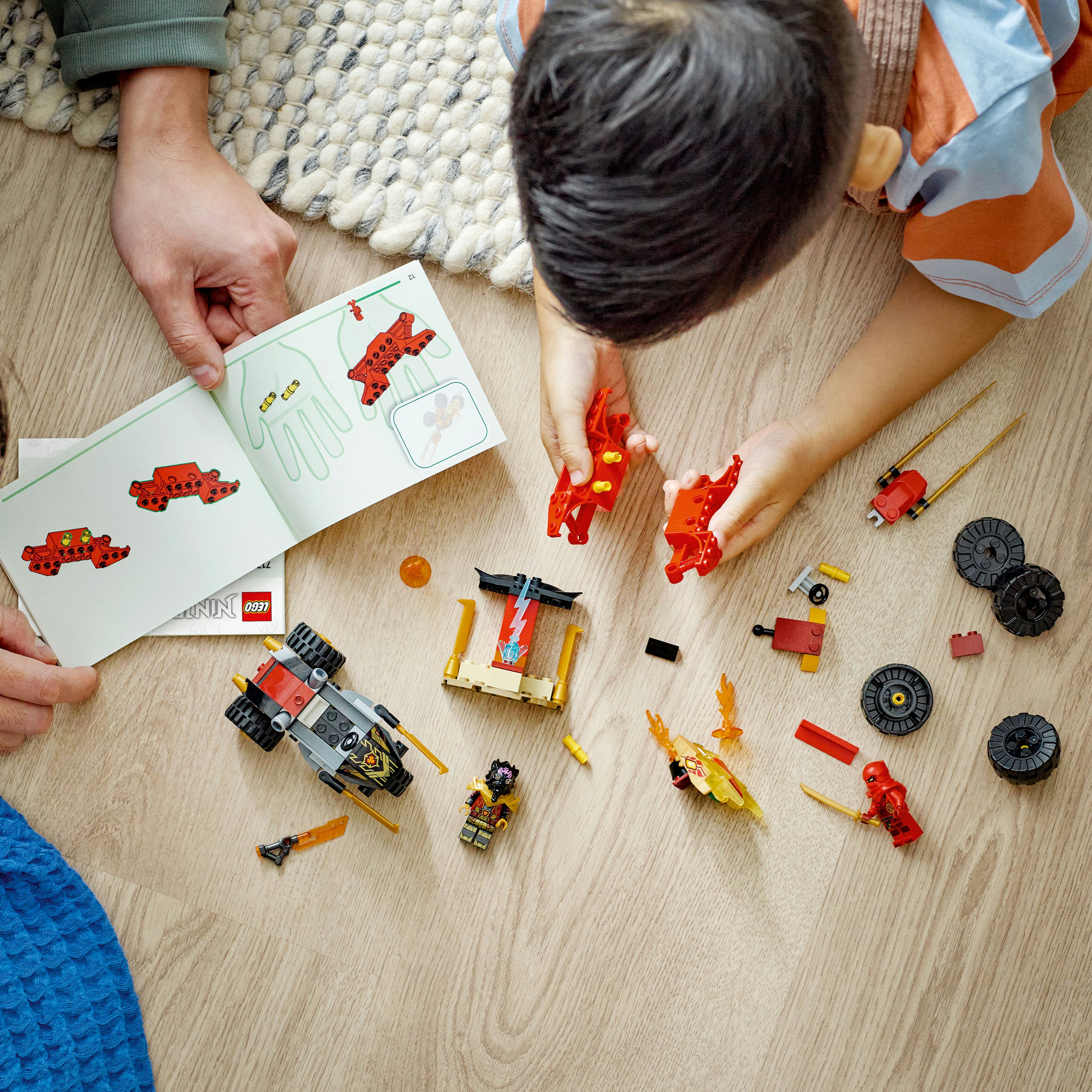 Handen die een rode LEGO-auto in elkaar zetten met instructies, diverse onderdelen op hout.