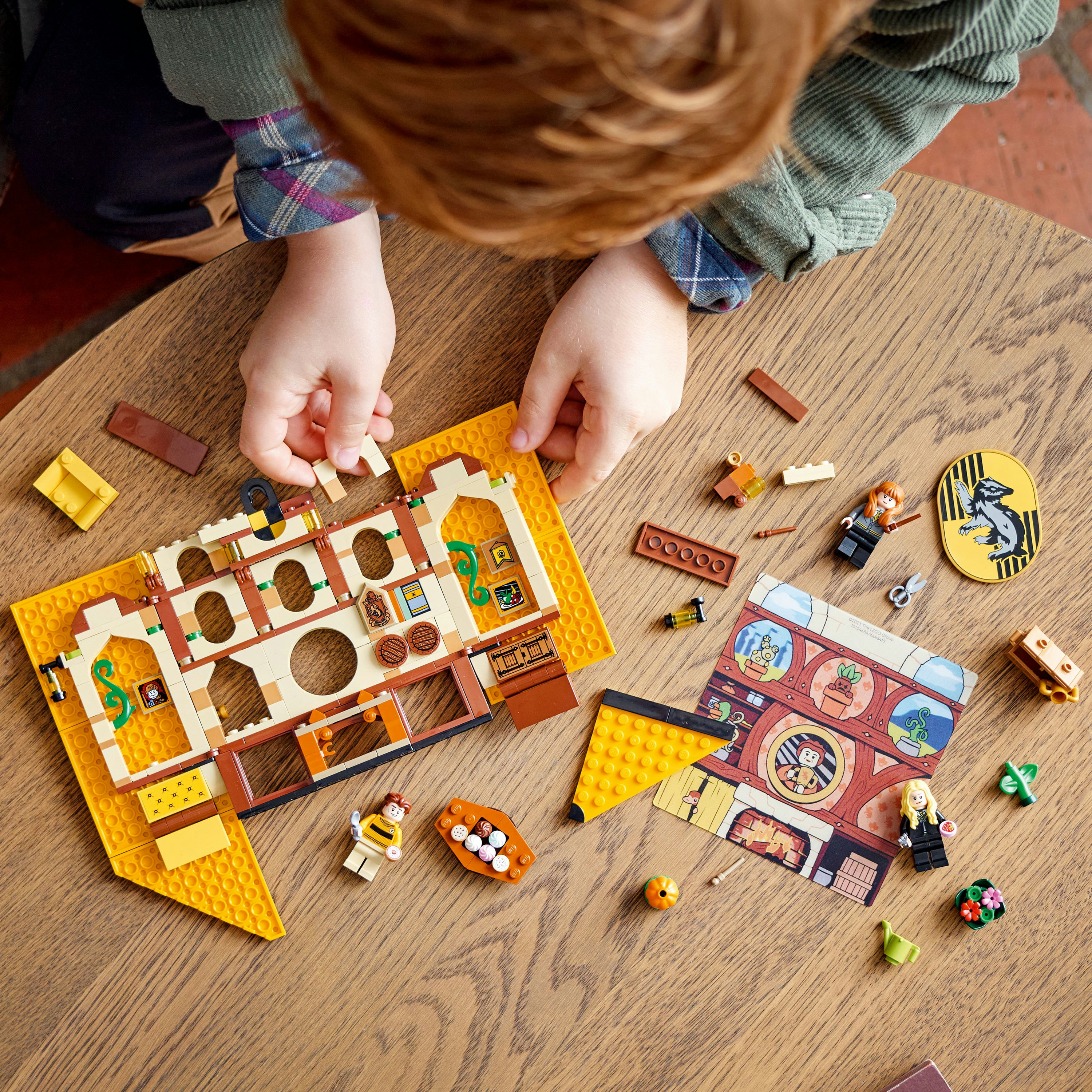 Ein Kind baut ein LEGO-Set. LEGO-Teile, darunter Minifiguren, liegen auf einem Holztisch.
