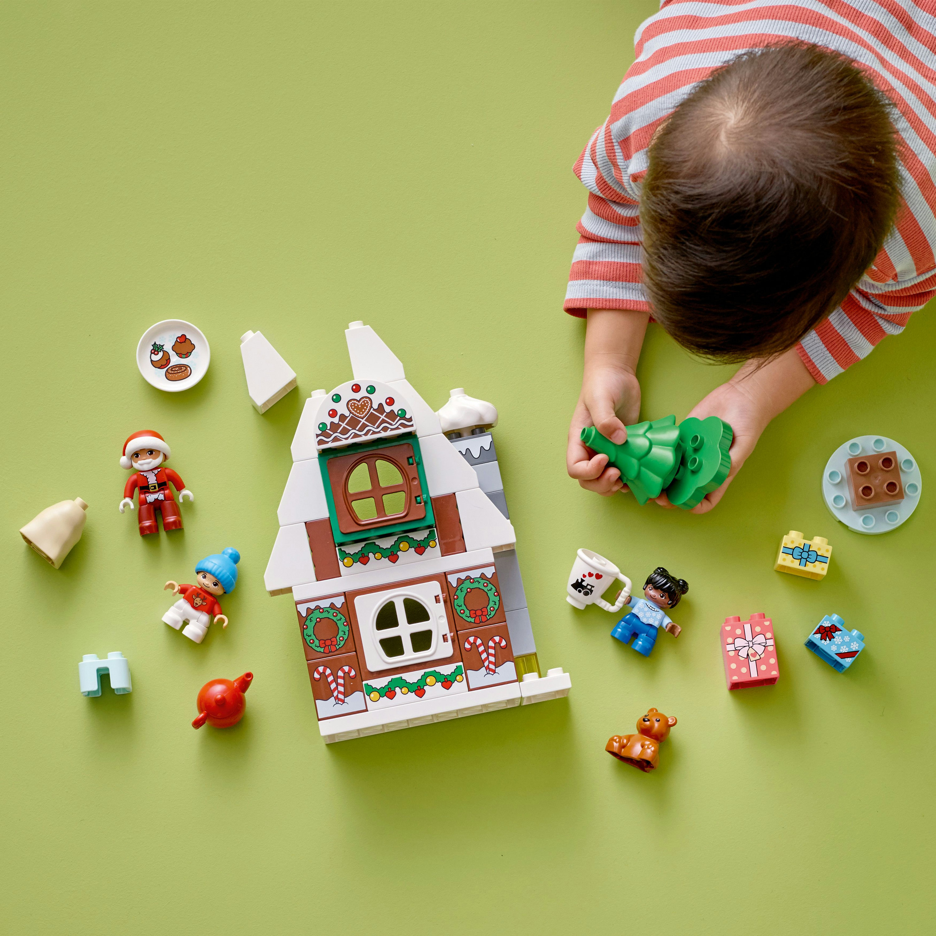 Un niño juega con un set de Navidad Lego Duplo, que incluye una casa, Papá Noel y regalos sobre verde.