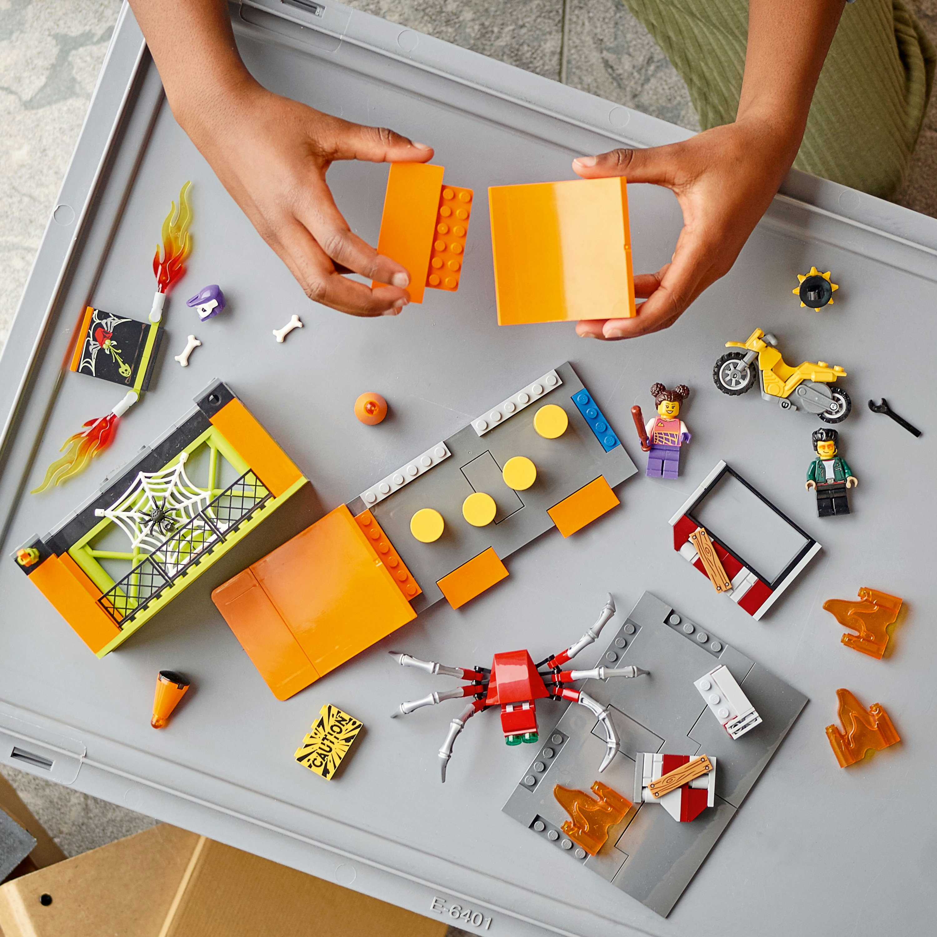 Componentes del set LEGO en una bandeja gris, incluyendo bloques naranjas, minifiguras y una araña.