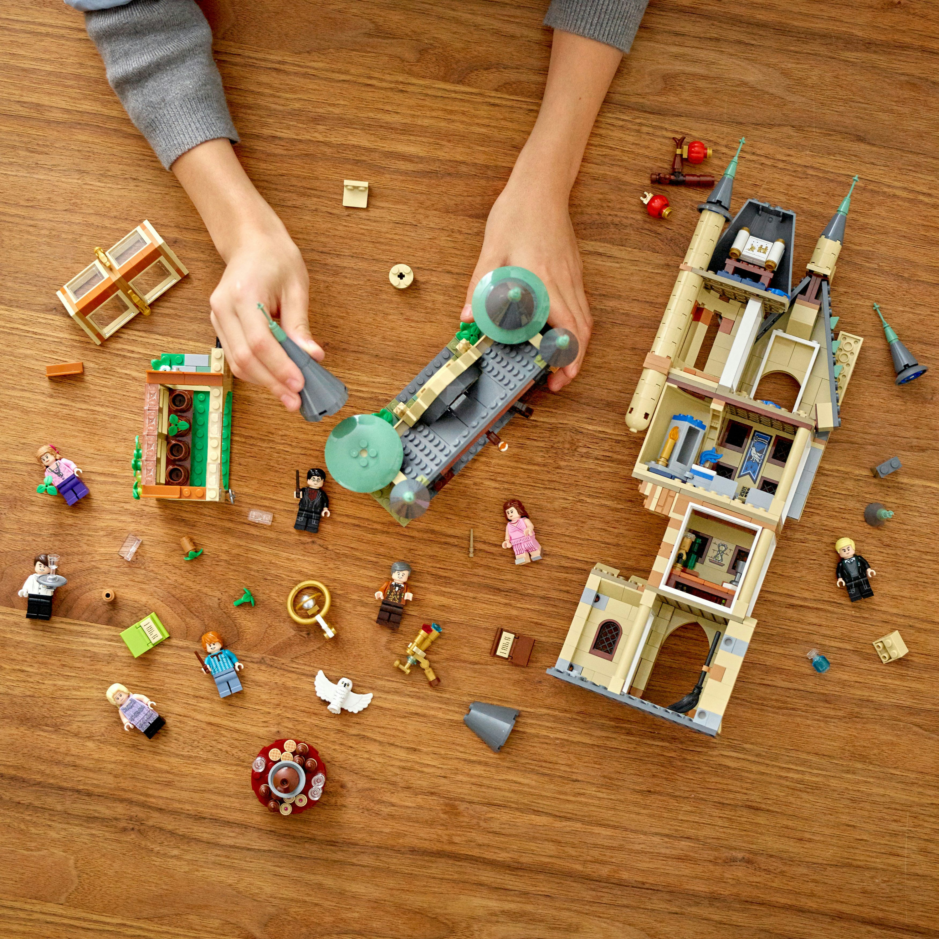 Vista dall'alto di un tavolo di legno con un set LEGO, che mostra le mani che assemblano vari componenti.