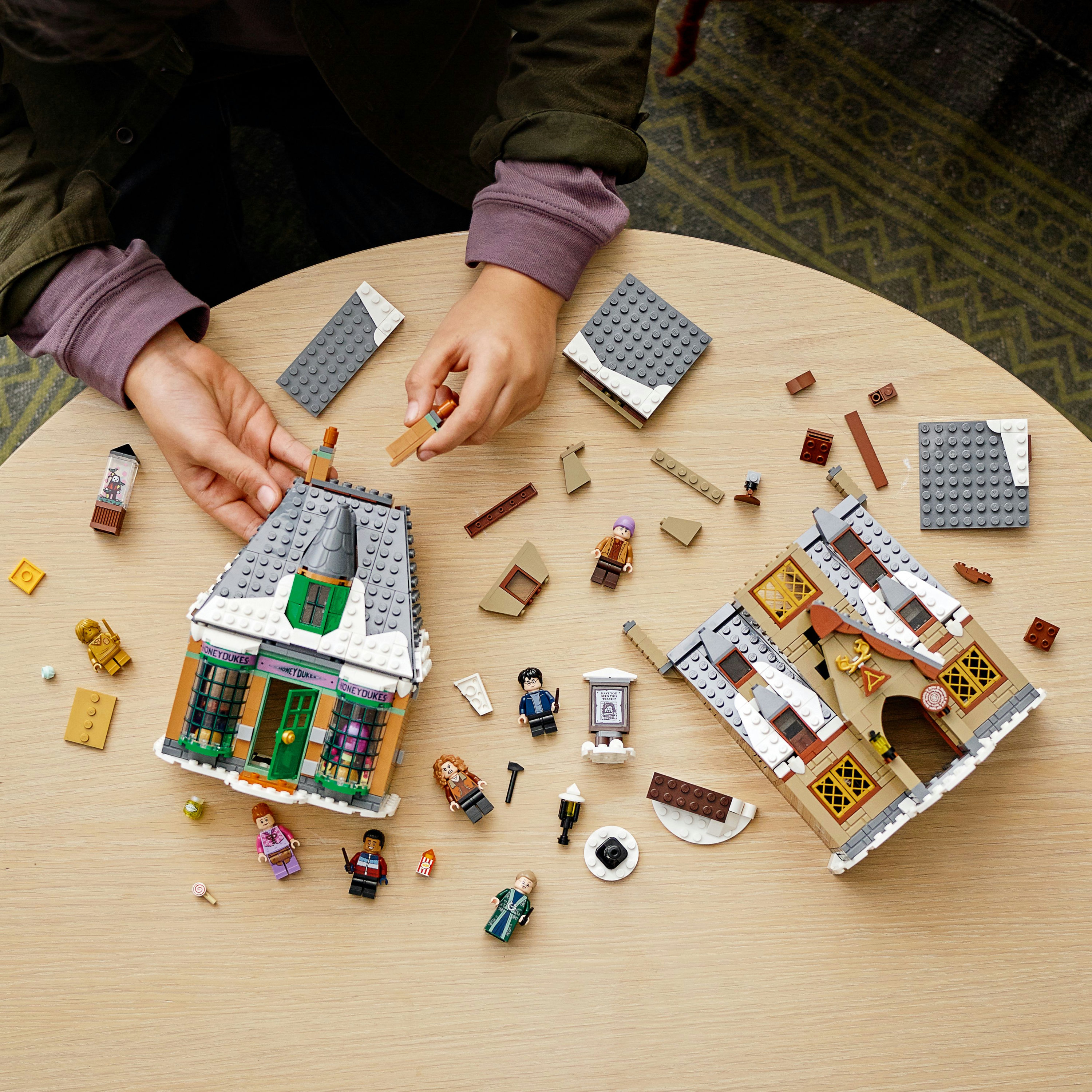 Hände, die Lego-Häuser mit Lego-Figuren und verschiedenen Lego-Teilen auf einer Holzoberfläche bauen.