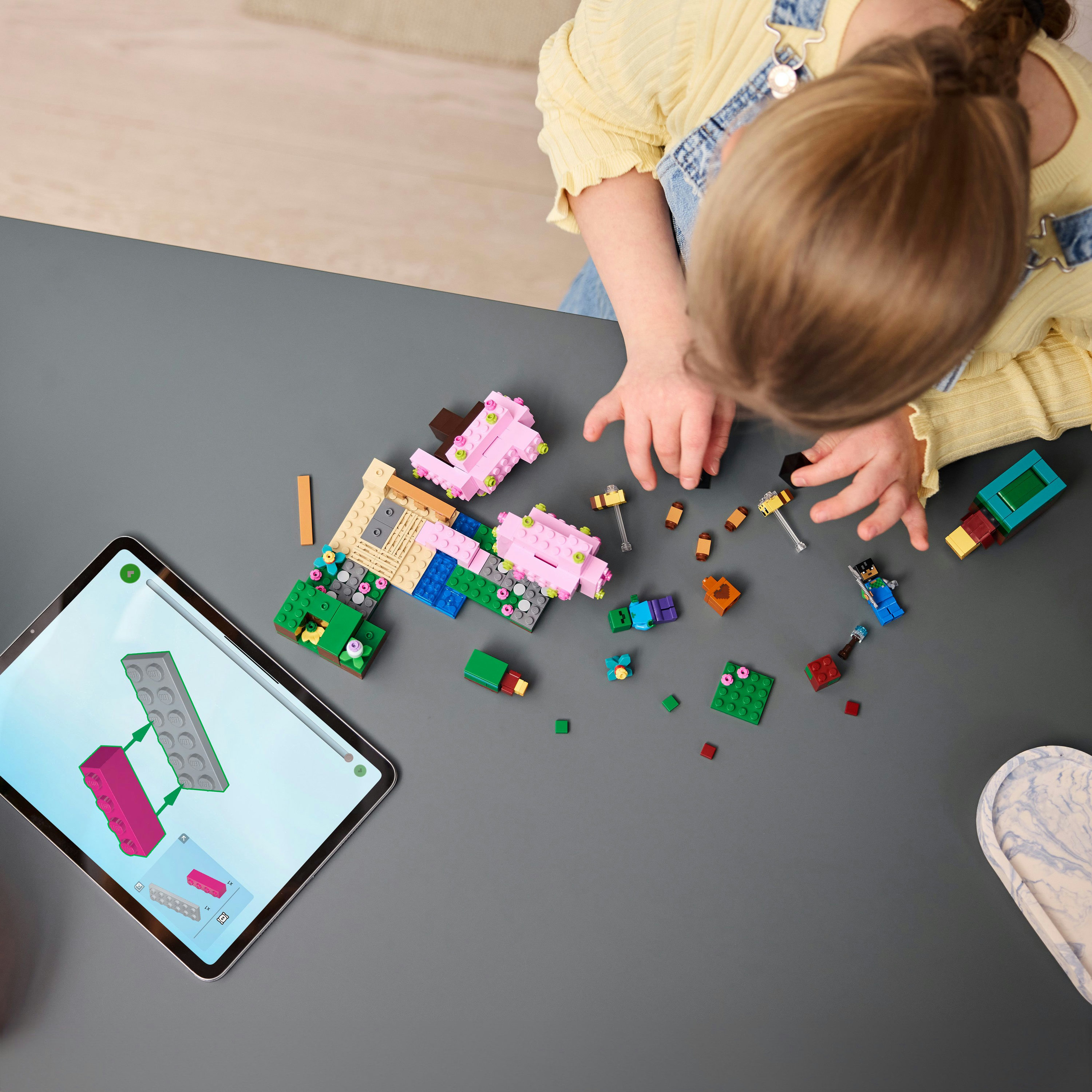 Een kind bouwt een Lego set op een grijs oppervlak. Een tablet toont de instructies. Bovenaanzicht.