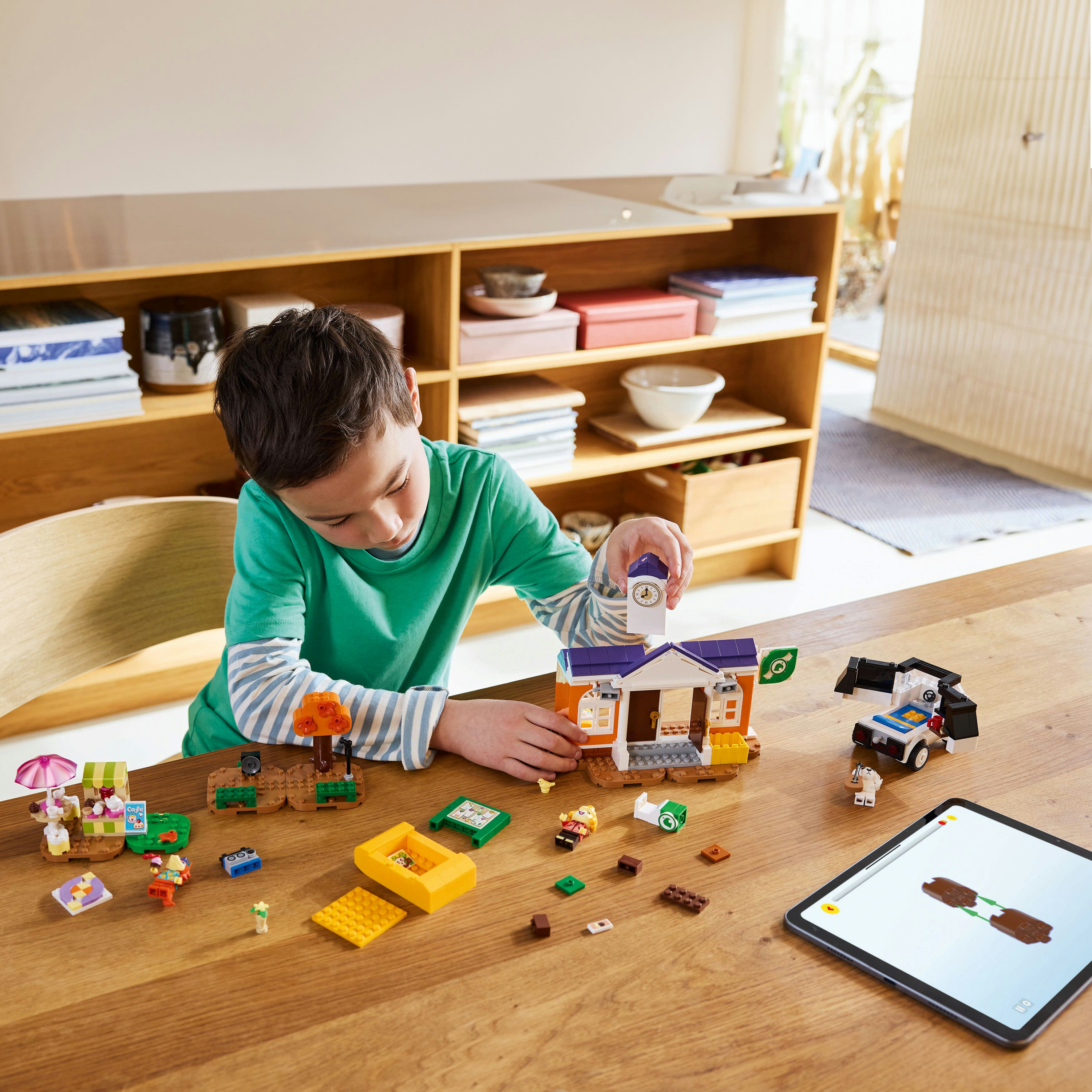 Bir çocuk Lego oynuyor. Küçük bir okul inşa ediyor. Masada başka Lego parçaları var.