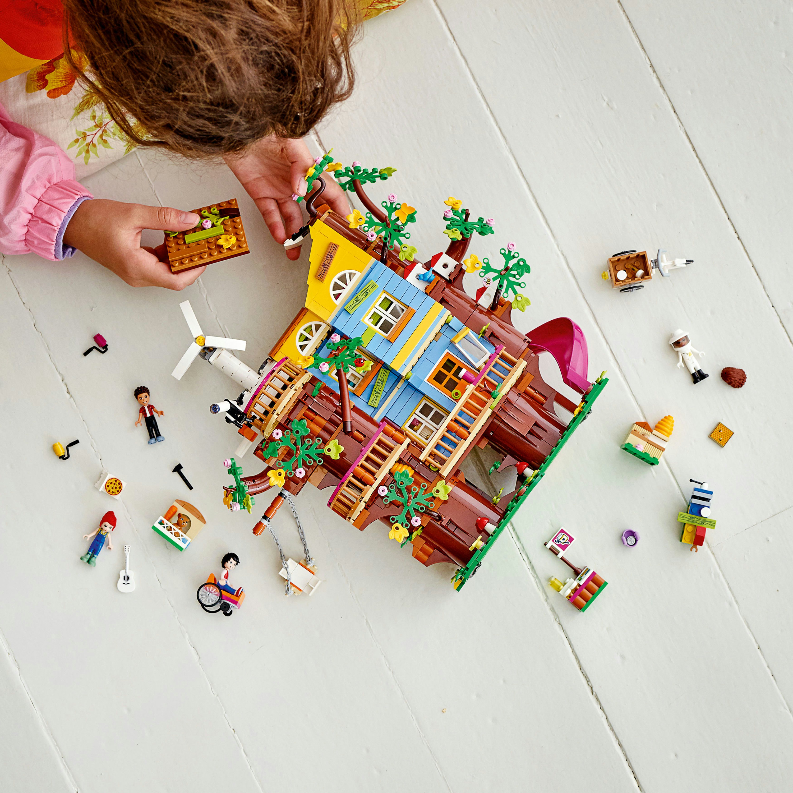 Ein Kind baut ein LEGO-Baumhaus, mit verschiedenen LEGO-Teilen und Mini-Figuren.