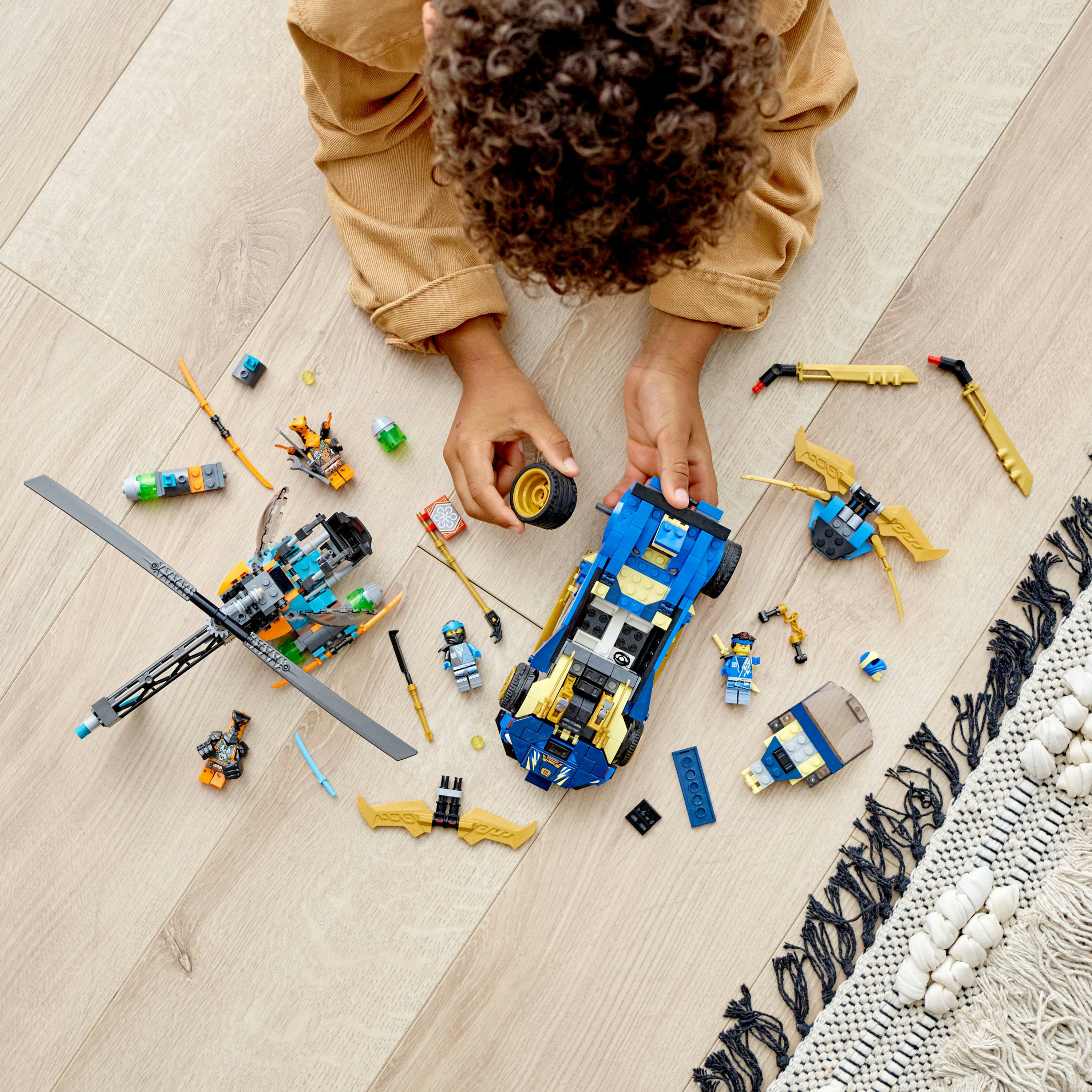 Un bambino con i giocattoli Lego Ninjago su un pavimento di legno. Sono visibili un'auto blu e un elicottero.