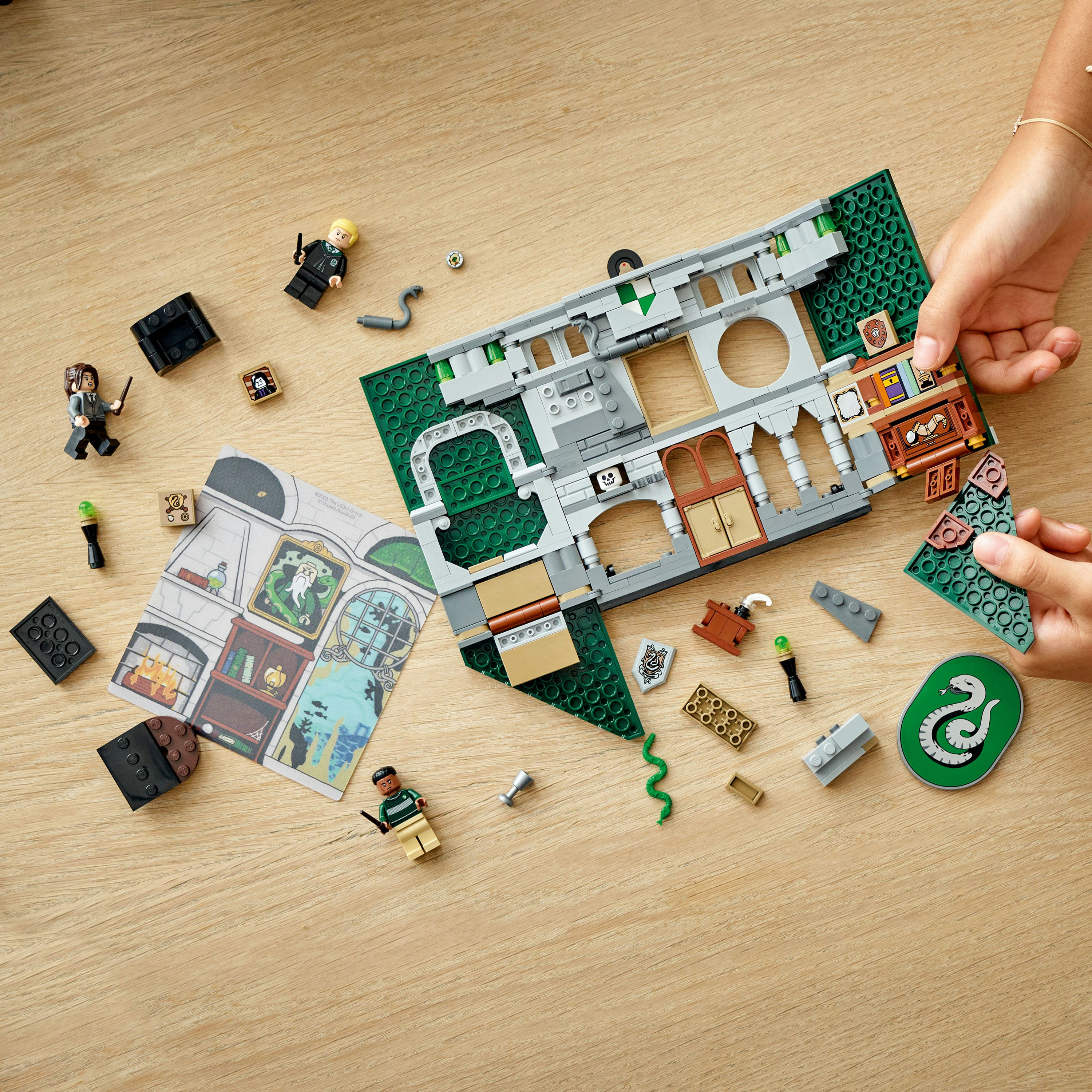 Lego-Set mit Mini-Figuren und Bausteinen auf Holzoberfläche. Hände bauen das Set zusammen.