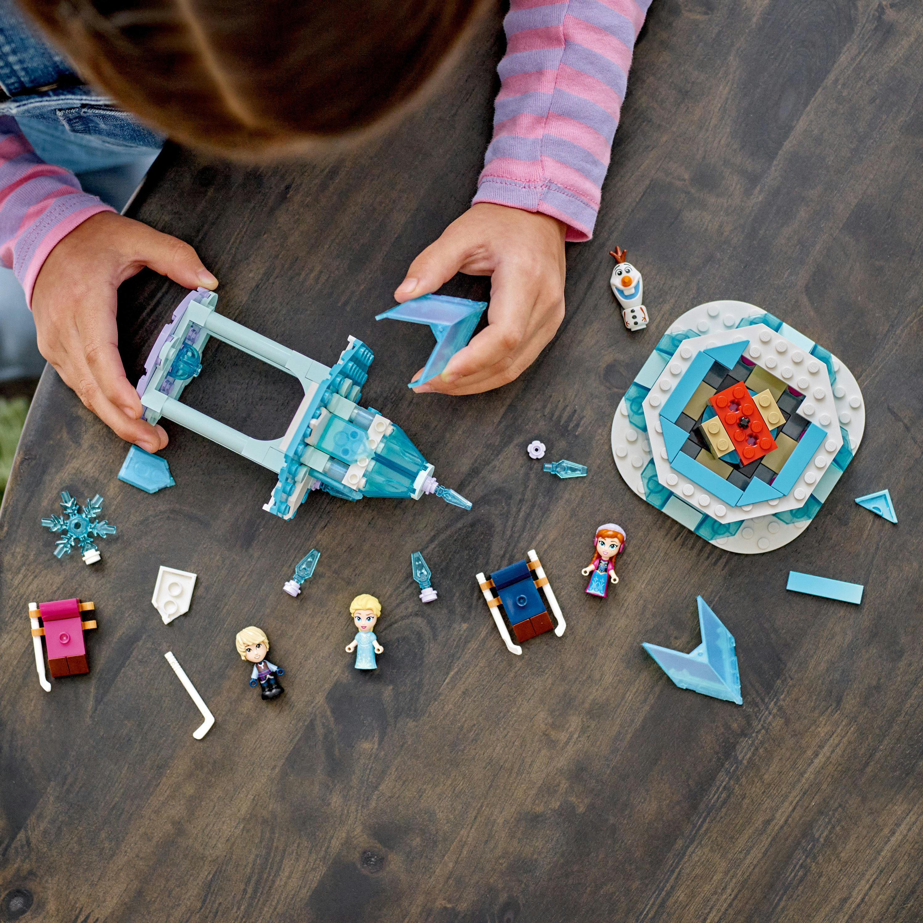 Manos montando un set Lego temático de Frozen, con Elsa, Anna, un castillo y varios elementos de hielo.
