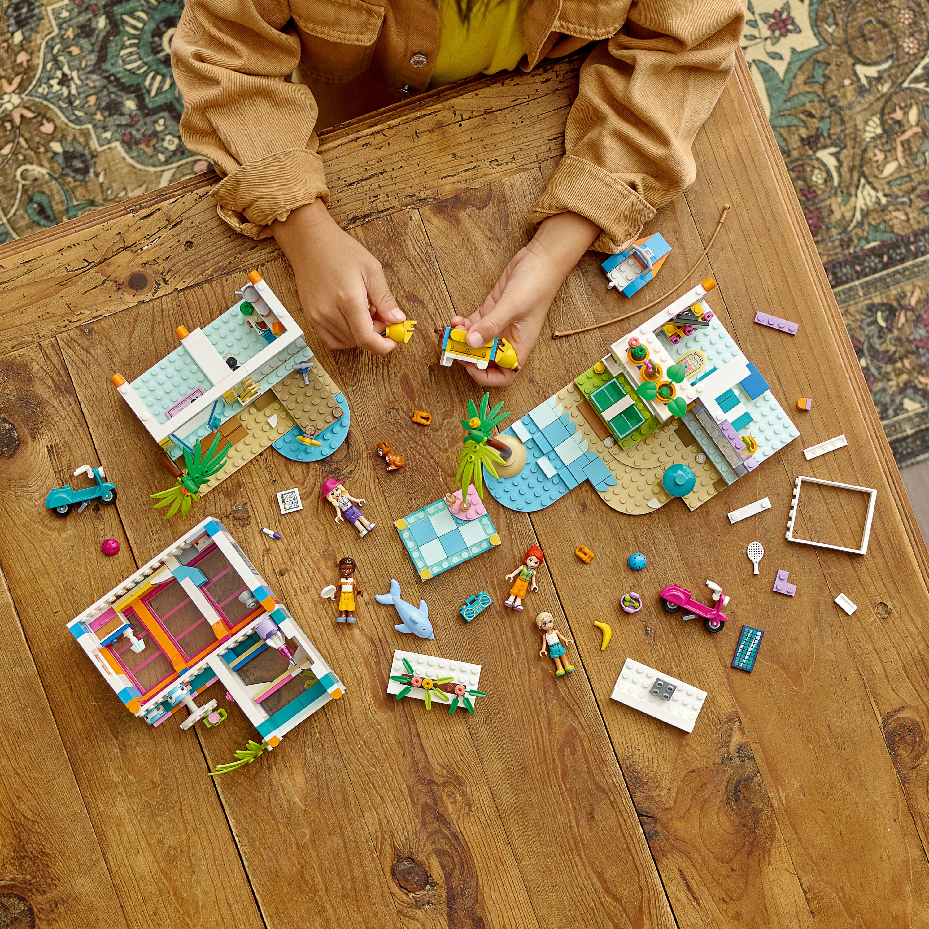 Kind speelt met Lego-sets. De scène bevat Lego-huizen en Lego-figuren op een houten tafel.