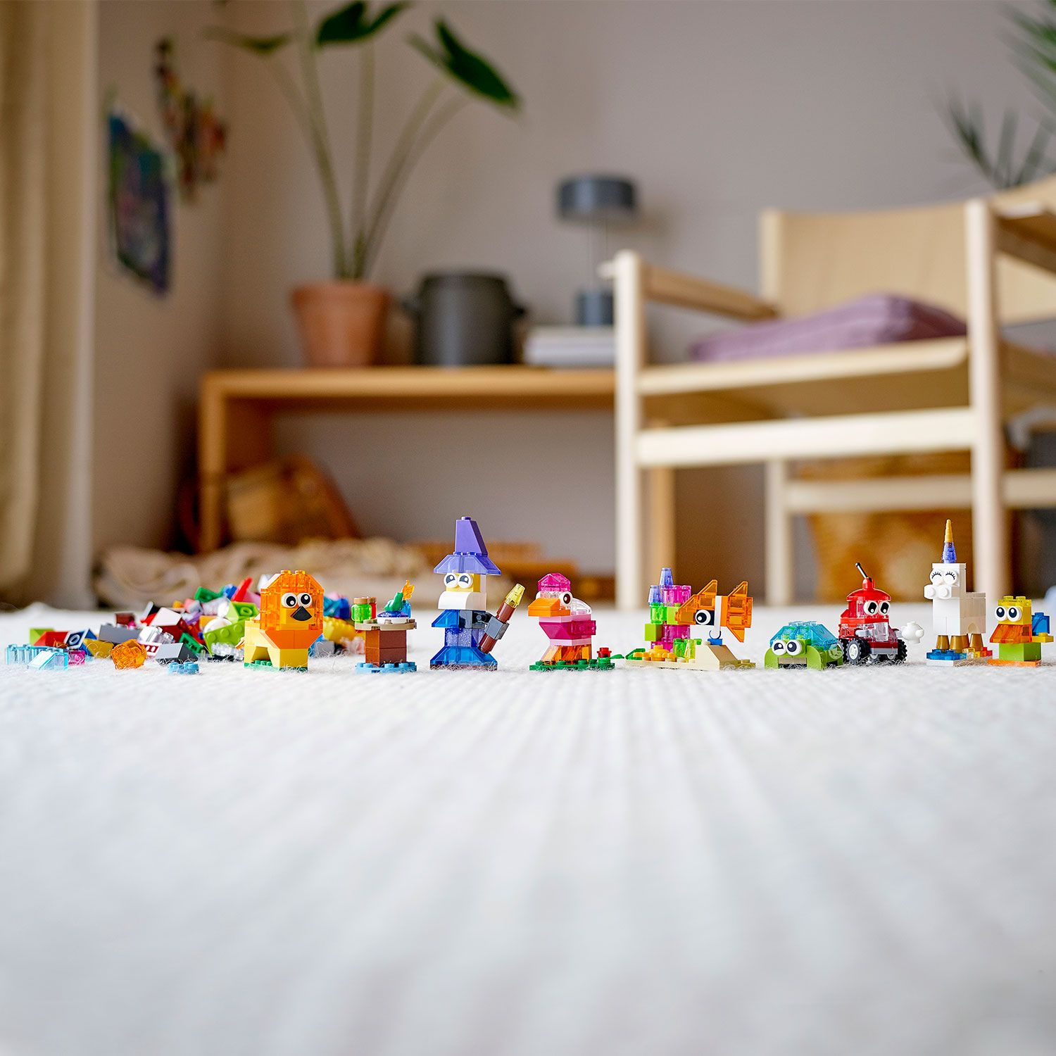 Beyaz bir halı üzerinde çeşitli hayvan benzeri figürler ve yapılar dahil olmak üzere renkli LEGO kreasyonları.