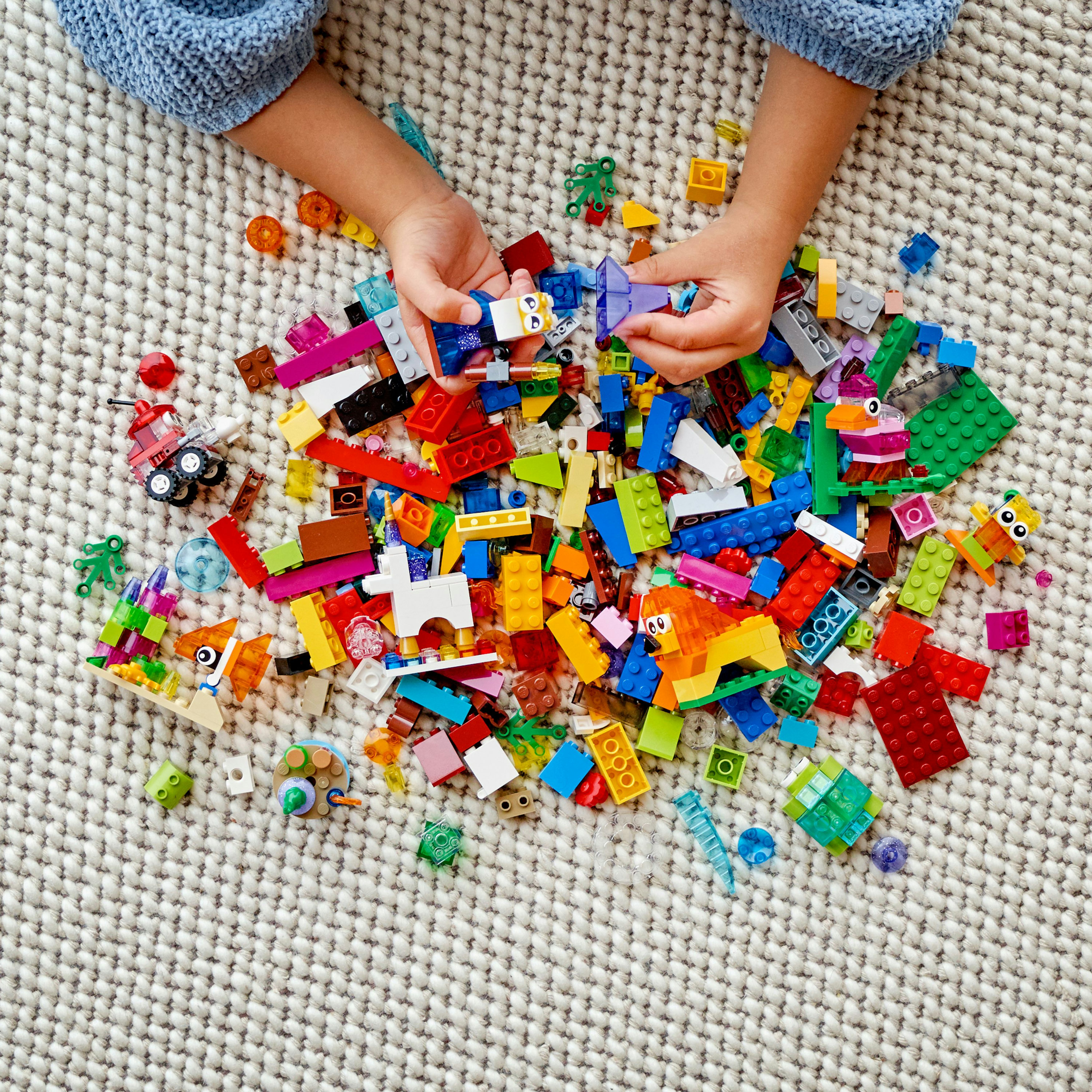 Bir çocuğun elleri, halı üzerinde çeşitli renkli LEGO bloklarıyla oynuyor.