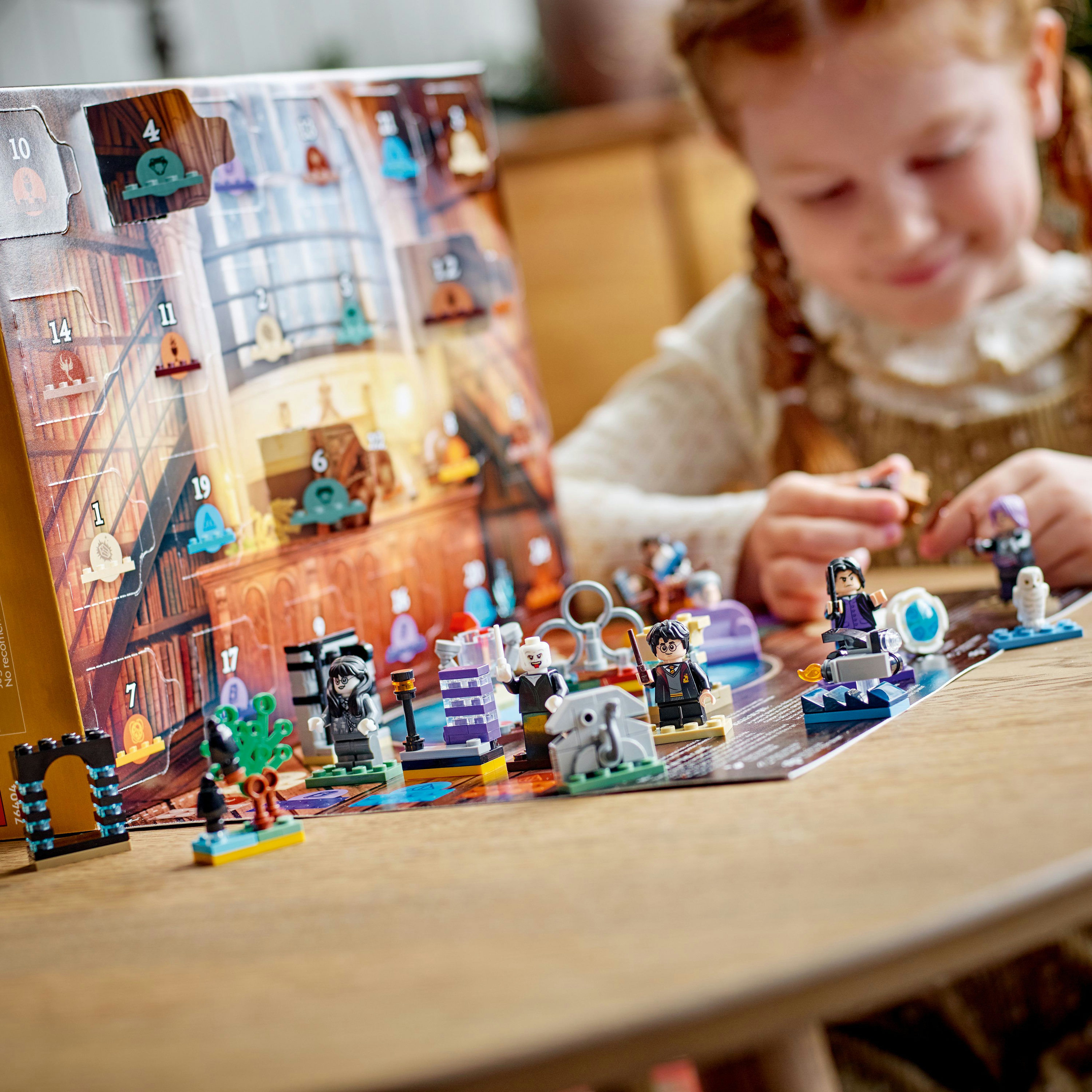 Een kind speelt met een LEGO Harry Potter Adventskalender. Minifiguren en kleine bouwwerken op een houten tafel.