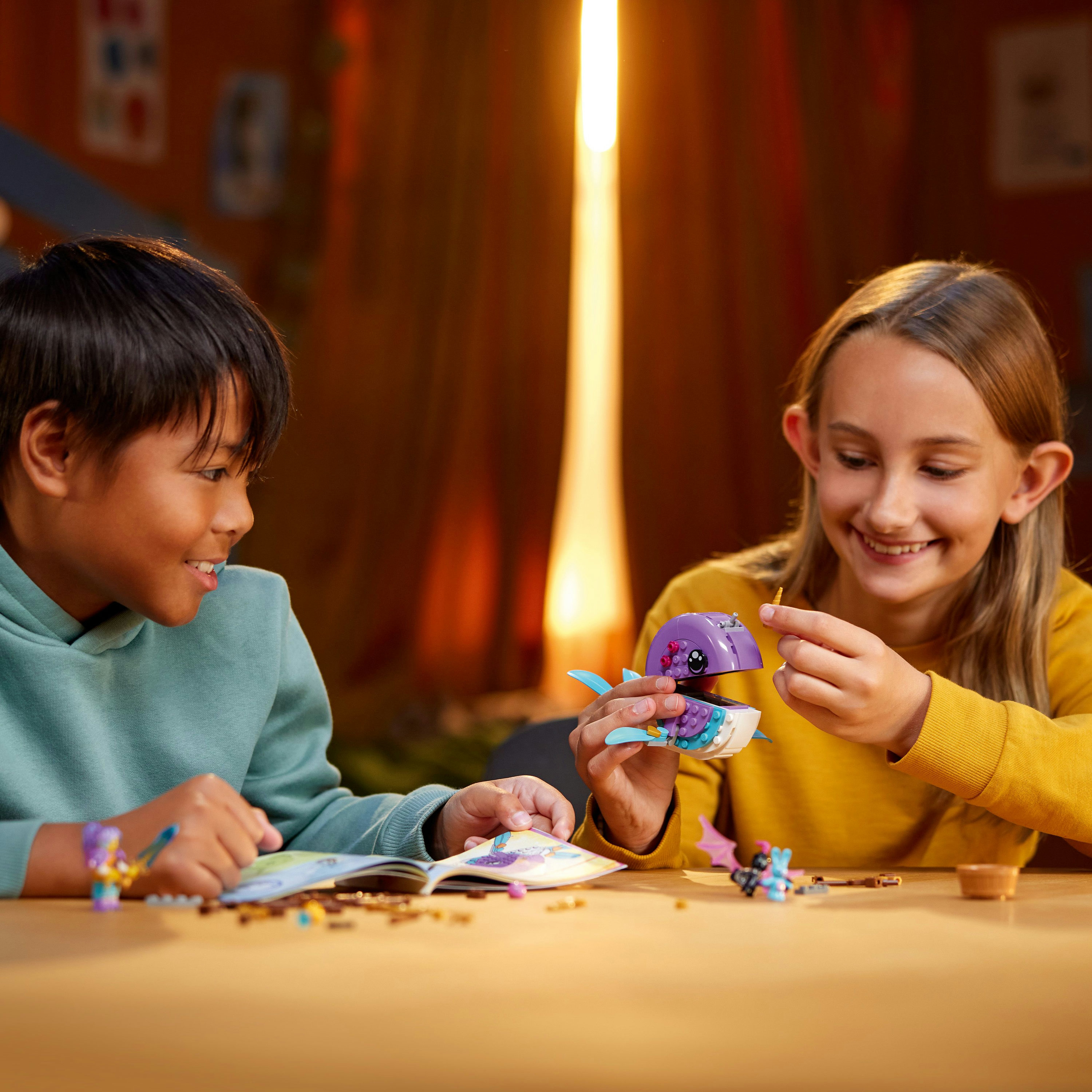 Zwei Kinder bauen ein lila Spielzeug. Einer hält das Spielzeug, der andere schaut ein Buch mit Teilen an.