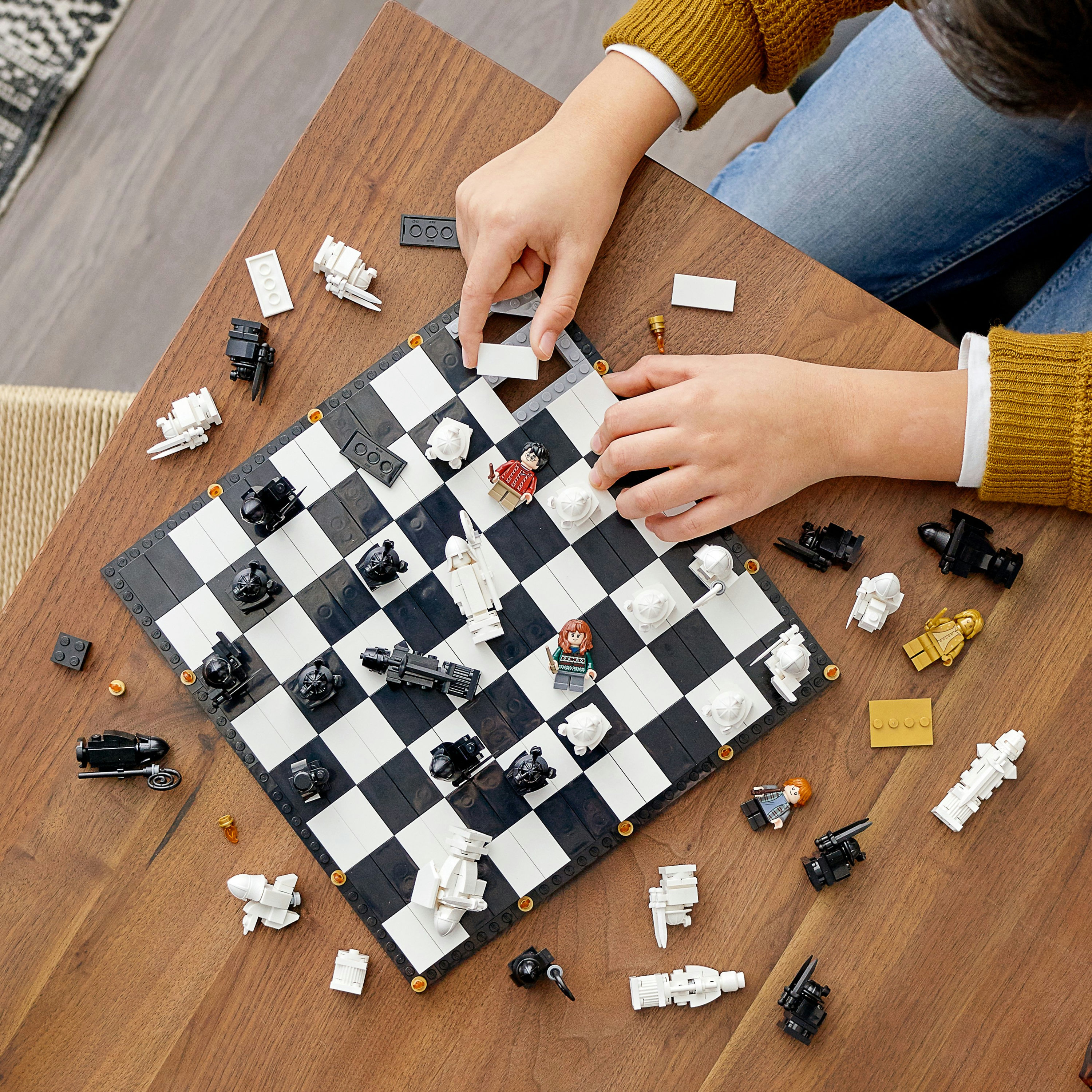Hände spielen Schach auf einem Lego Schachbrett. Schwarz-weiße Quadrate mit Lego Schachfiguren. Holztisch.