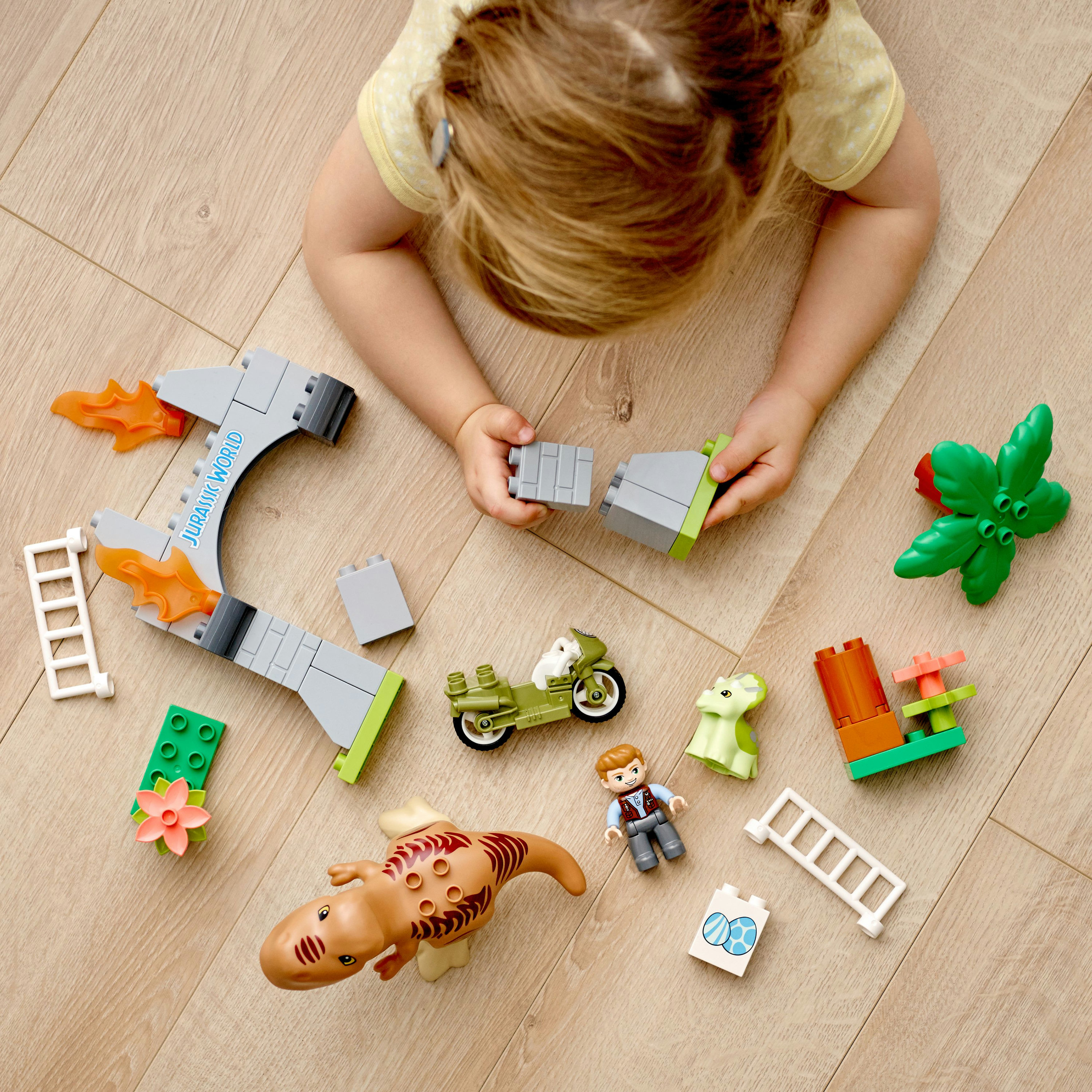Un bambino gioca con Lego Duplo, creando una scena di Jurassic World con dinosauri e una moto.