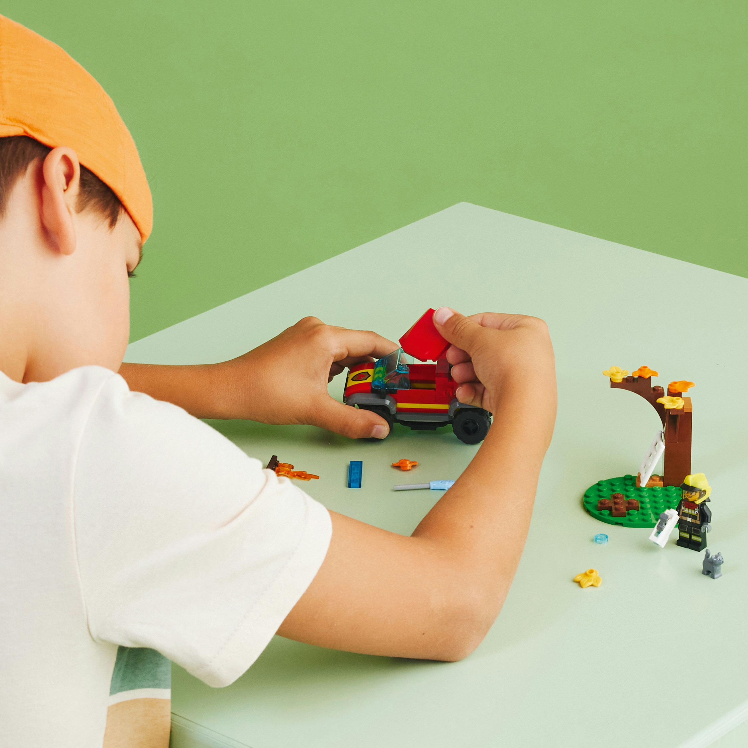 Kind spielt mit Lego. Rotes Auto, Baum und Figur. Grüner Tisch, grüner Hintergrund.
