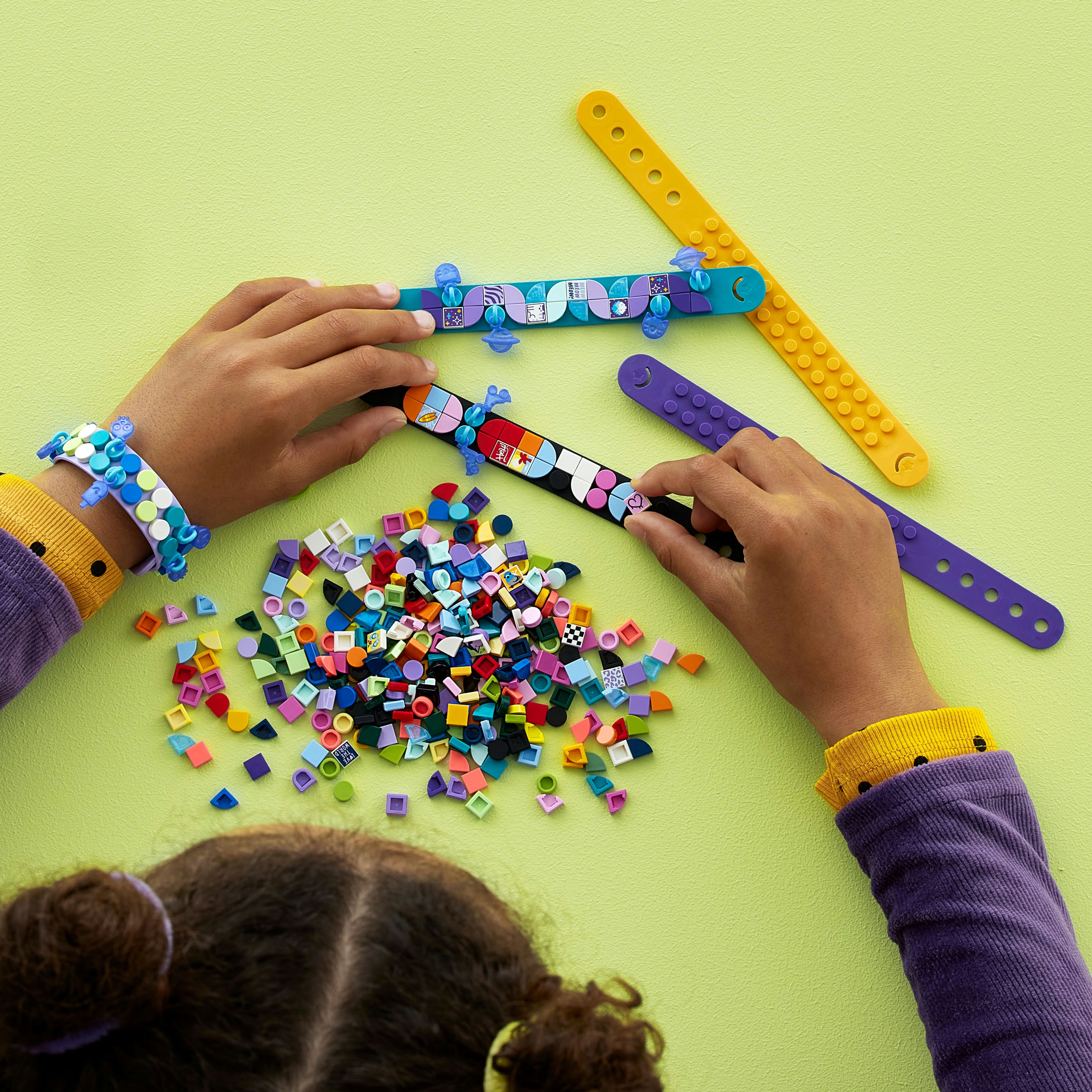 Manos construyendo pulseras coloridas con muchos pequeños ladrillos Lego.