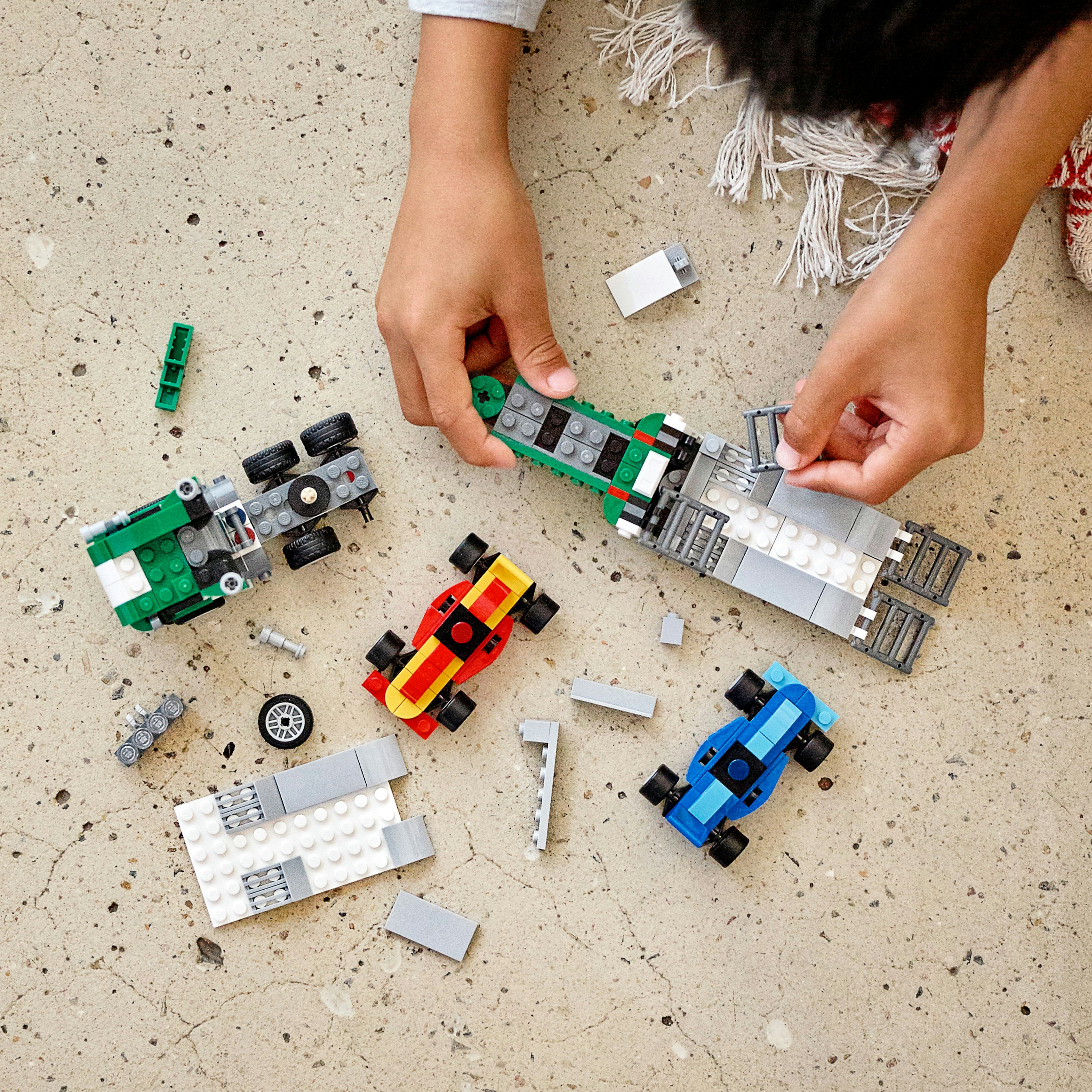 Kinderhände, die Lego-Autos zusammenbauen. Mehrere Autos in Rot, Grün und Blau sind teilweise auf Beton gebaut.