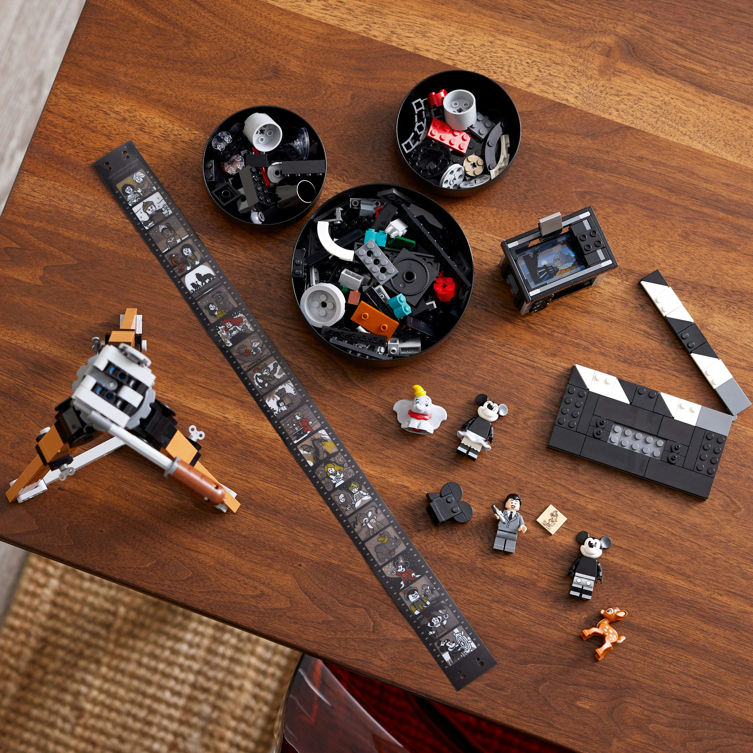 Zestaw do budowy scen Lego z rolką filmową, klapsem i różnymi minifigurkami na drewnianym stole.