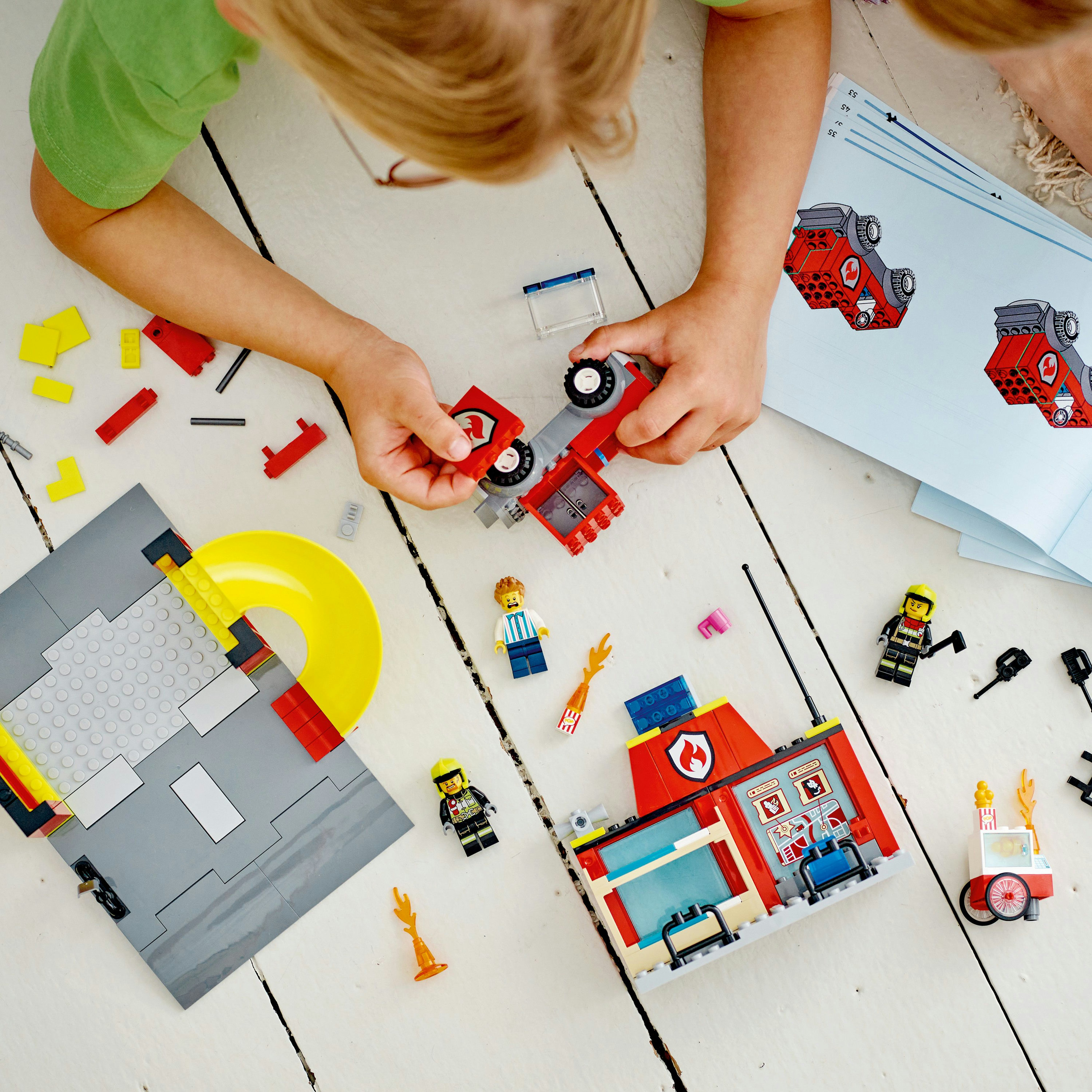 Niño construyendo una estación de bomberos roja con piezas de Lego, incluye figuras de bomberos.