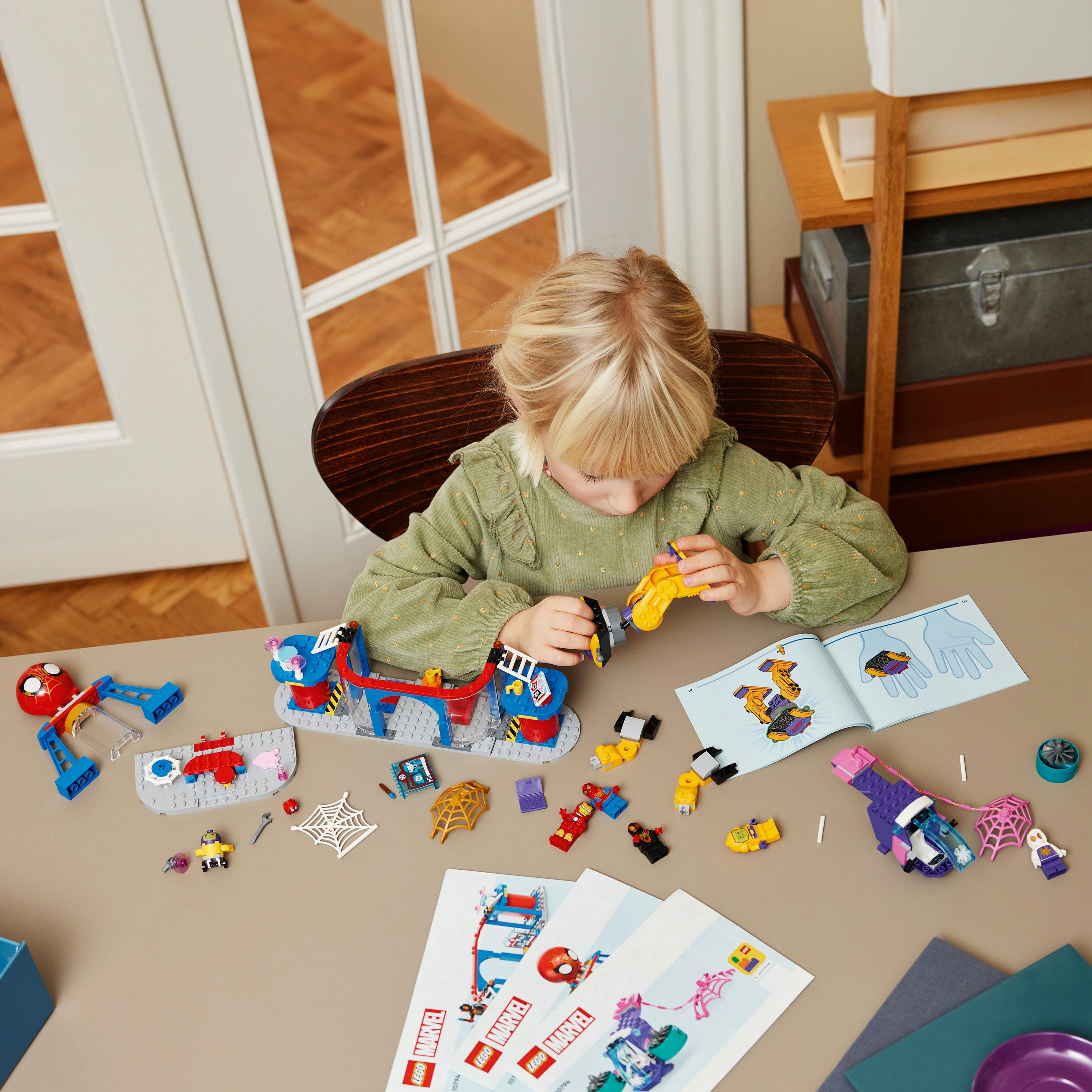 Un bambino gioca con un set Lego su un tavolo. Il set include personaggi, una ragnatela e un edificio.