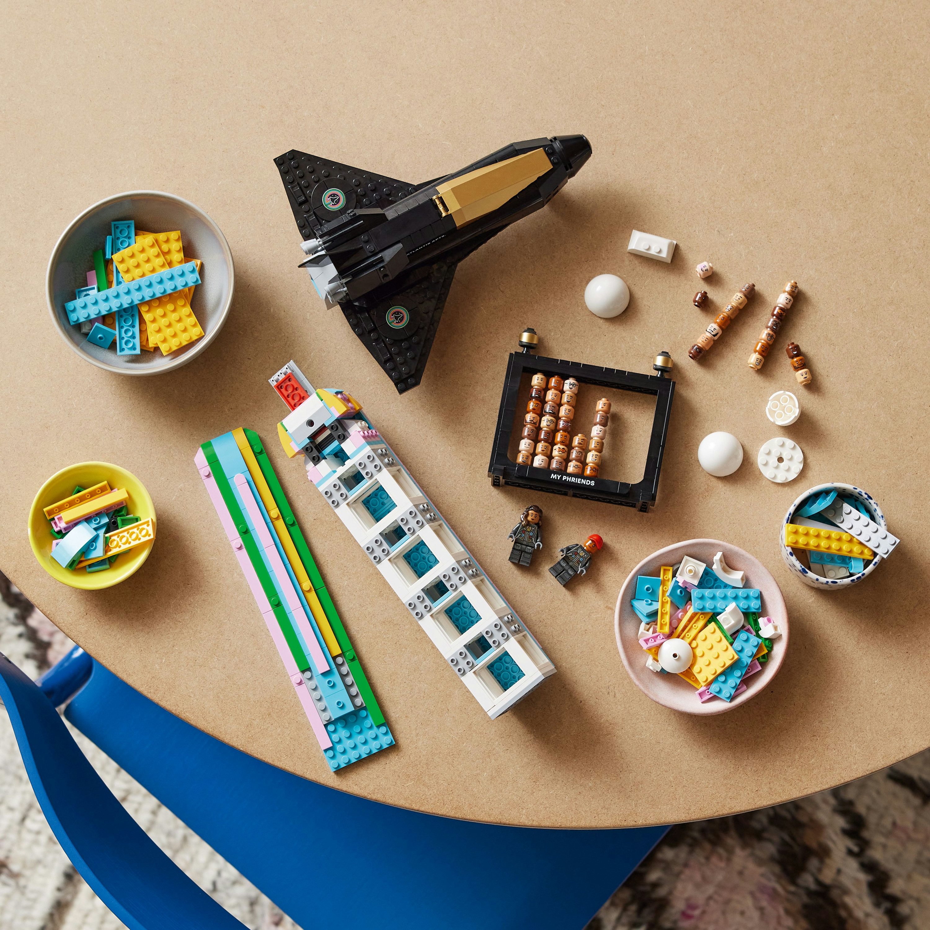 Klocki LEGO na stole: samolot, klocki, miski, figurki. Różne kolory.