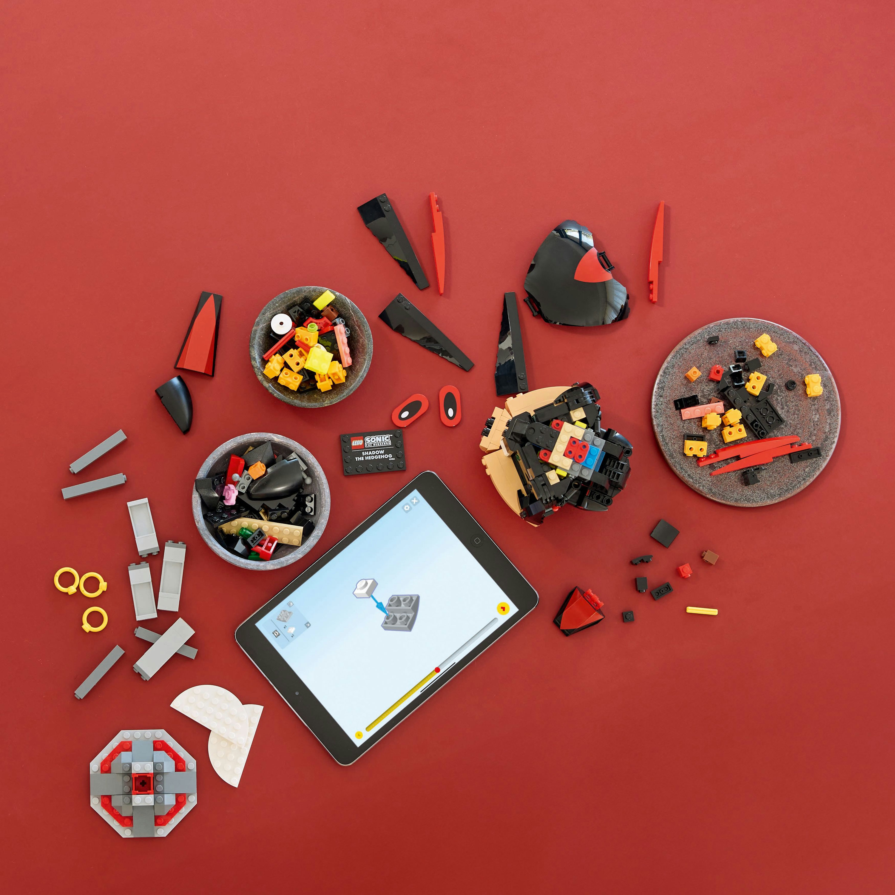 Kırmızı bir yüzeyde LEGO parçaları ve talimatları gösteren bir tablet, çeşitli LEGO parçaları.