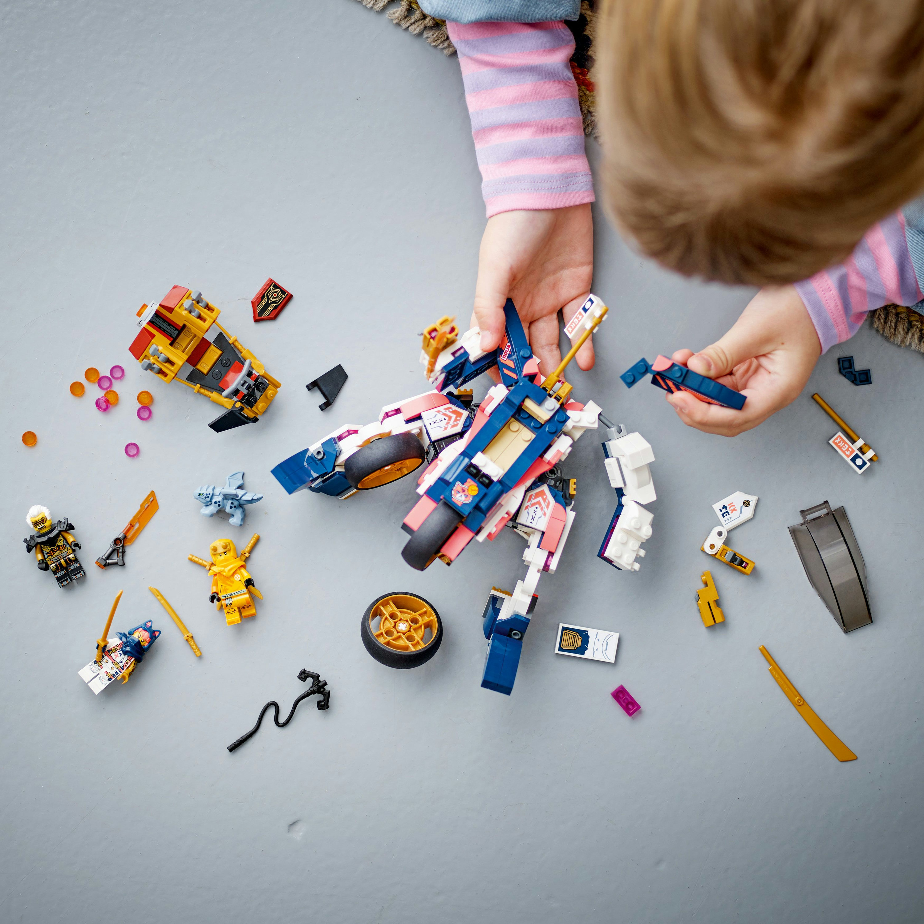 Un bambino gioca con set Lego, assemblando un mech e altri pezzi.