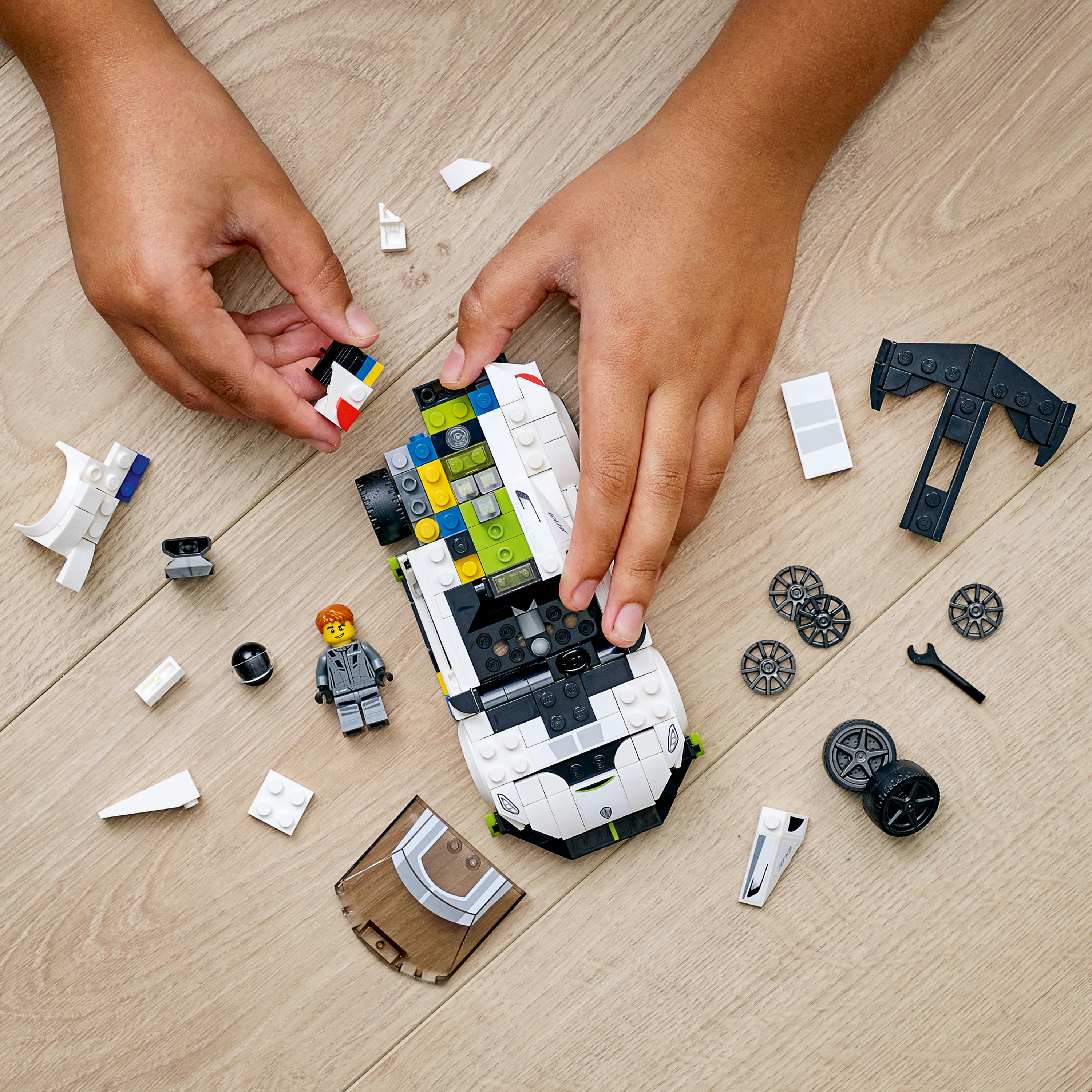 Hände, die ein weißes und grünes Lego-Rennwagen-Set auf einer Holzoberfläche zusammensetzen.