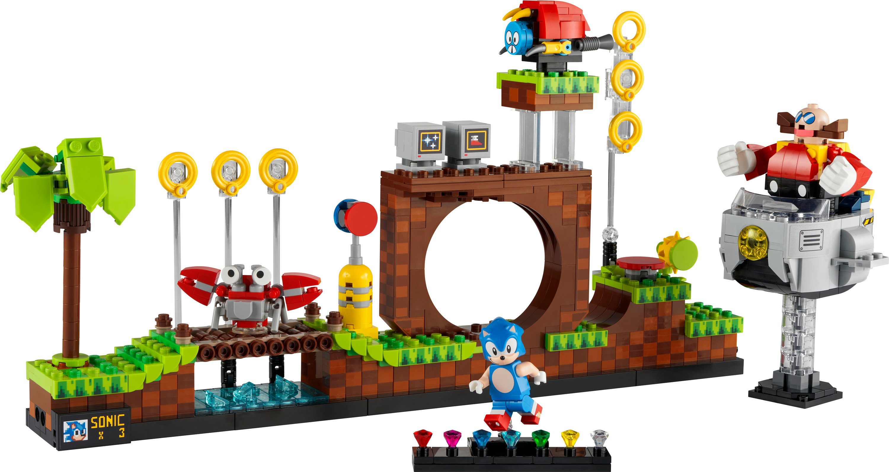 Zestaw Lego Sonic. Figurka Sonica na torze, robot, pierścienie i pojazd Eggmana na zielono-brązowej scenie.