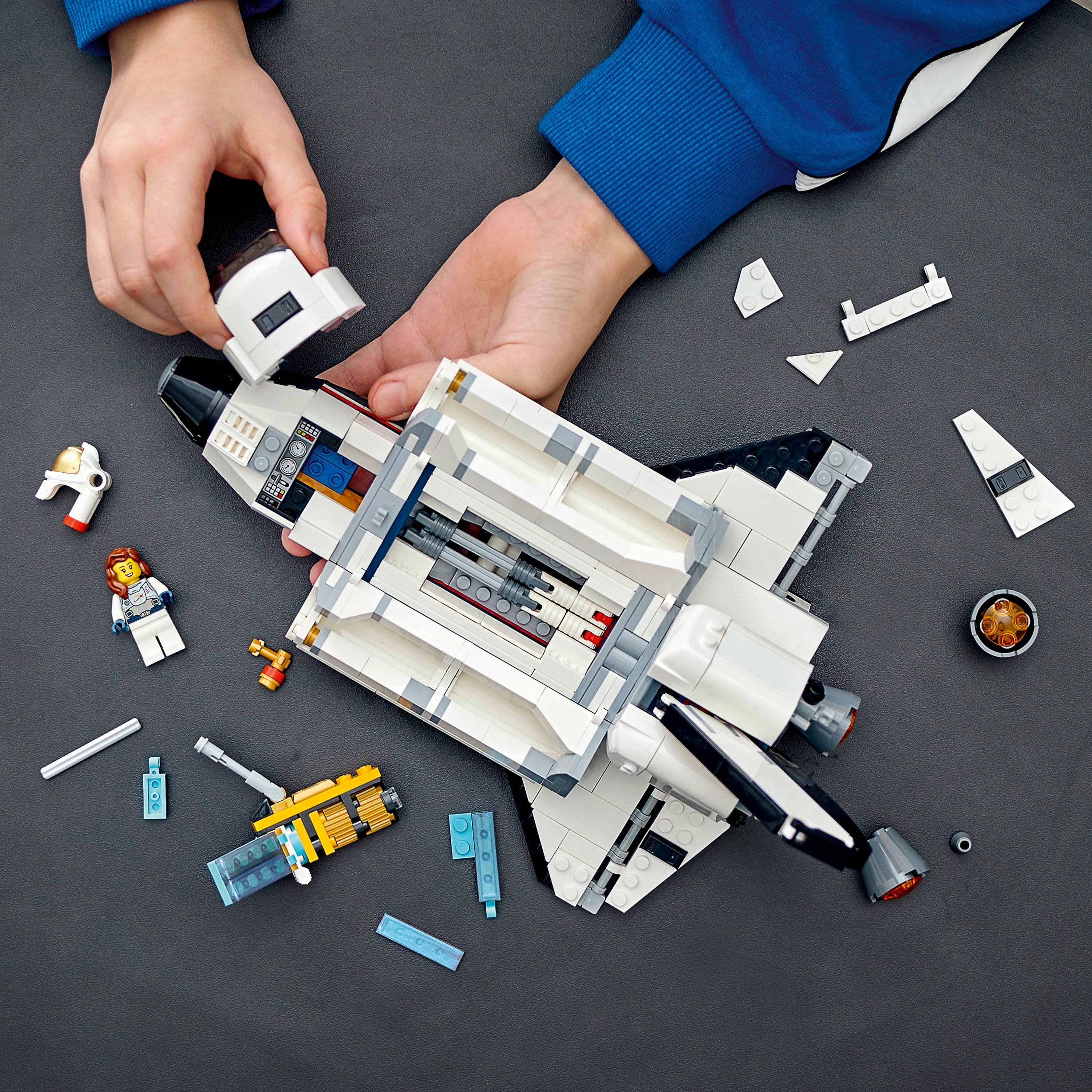 Hände, die ein LEGO-Weltraumschiff zusammensetzen. Teile und Minifiguren sind um das Shuttle verstreut.