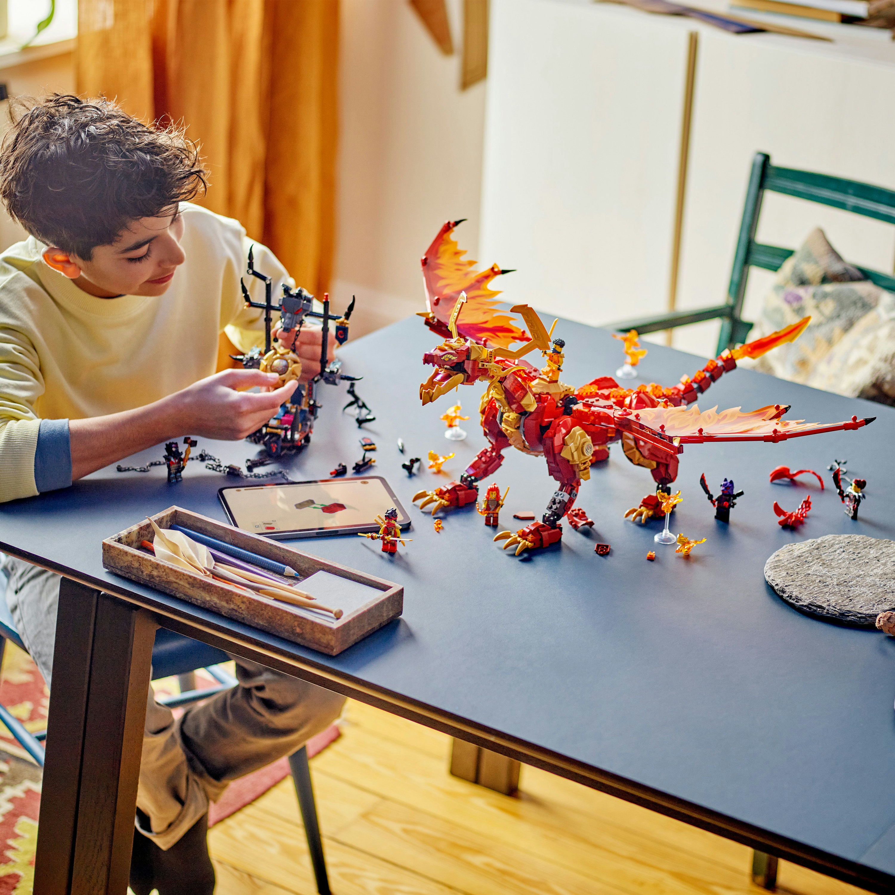 Chłopiec buduje smoka Lego otoczonego klockami i akcesoriami Lego na stole.
